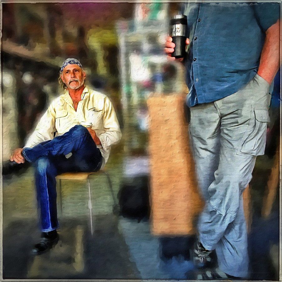 A man in a blue shirt is standing next to a man sitting on a stool