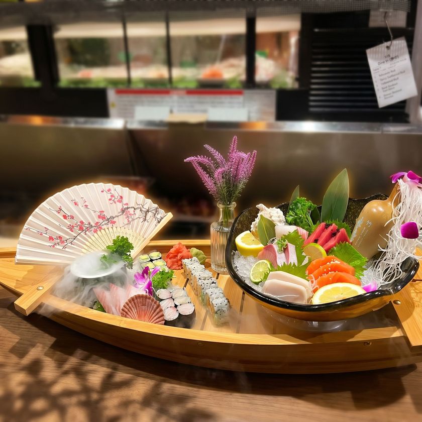 Artful sushi platter on a wooden boat with a decorative fan and flowers at a restaurant counter