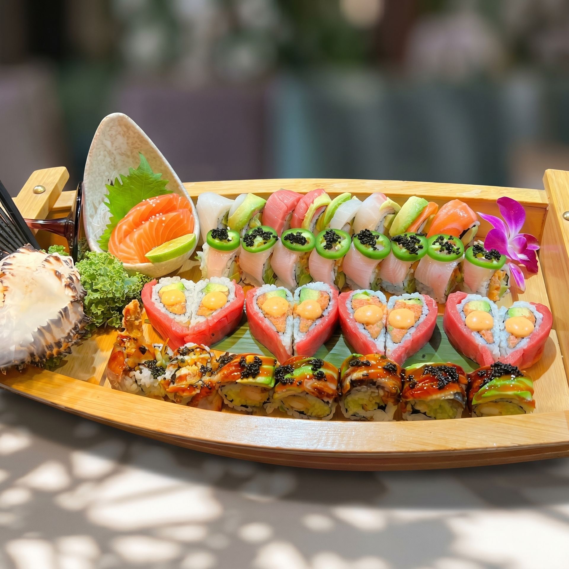 Colorful sushi platter on a wooden boat tray with avocado, salmon, tuna, and flower garnish