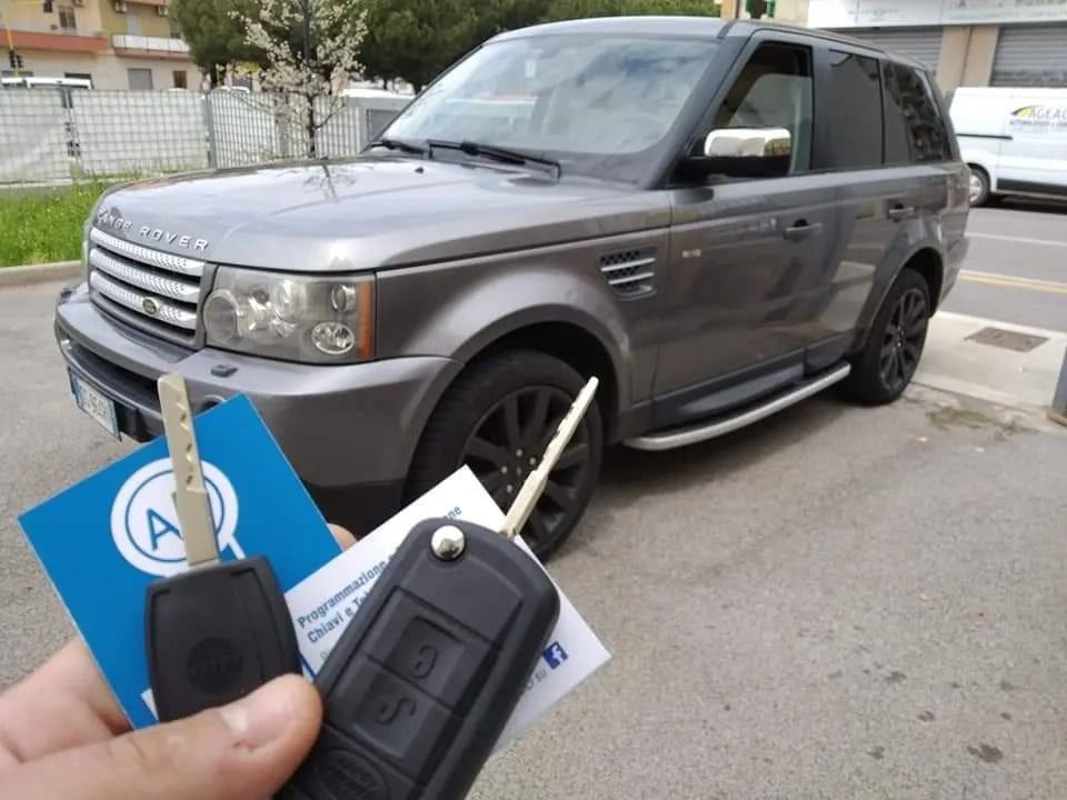 Persona che tiene le chiavi dell'auto davanti a un SUV Land Rover Sport grigio parcheggiato all'esterno.