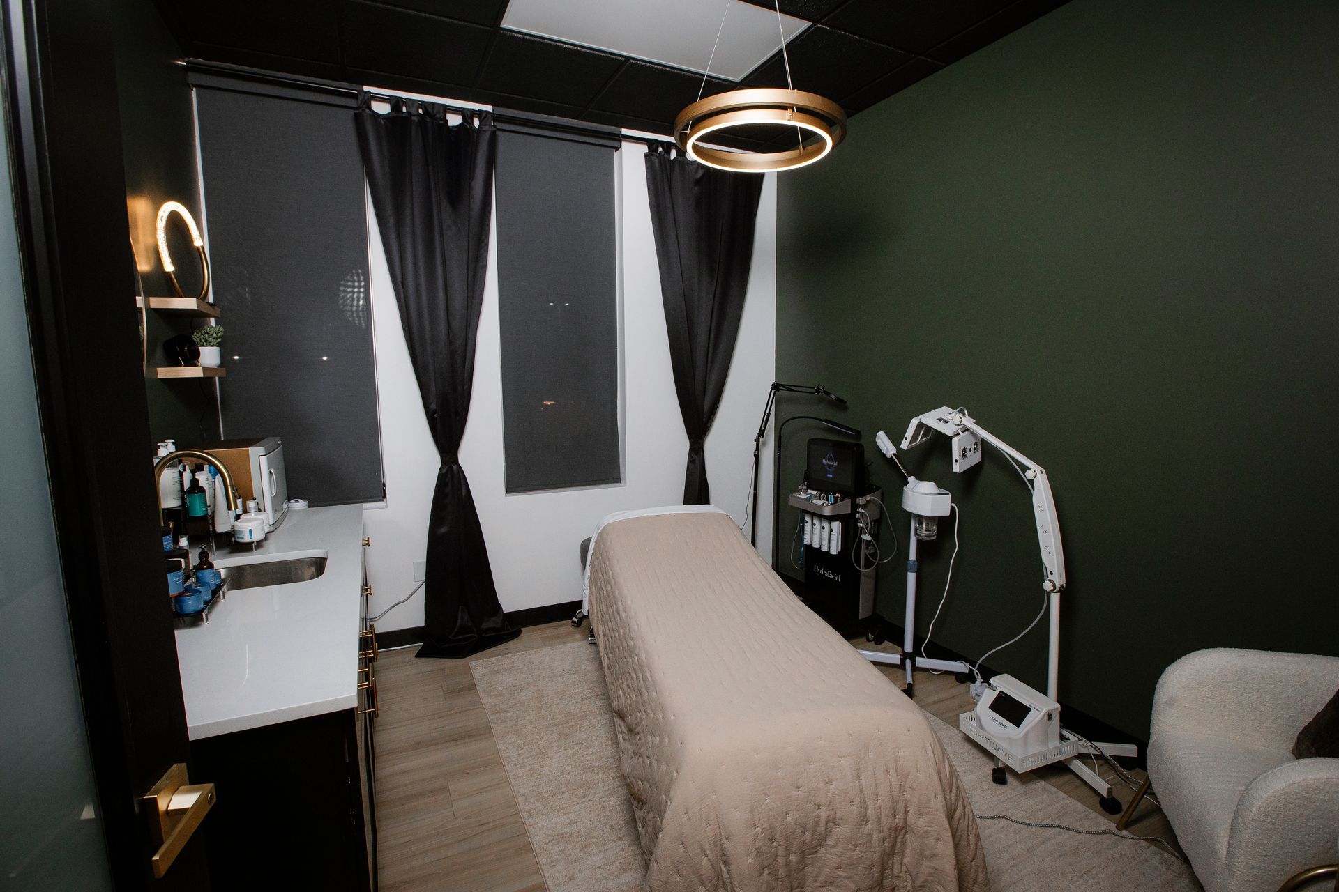 Small treatment room with massage table, black curtains, vanity desk, and exercise equipment.