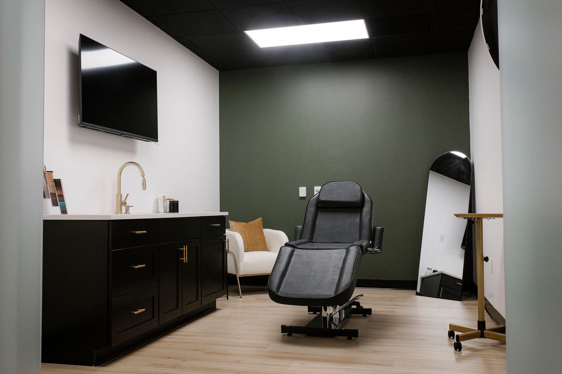 Modern office room with black chair, desk, wall-mounted TV, and mirror in a minimalist space