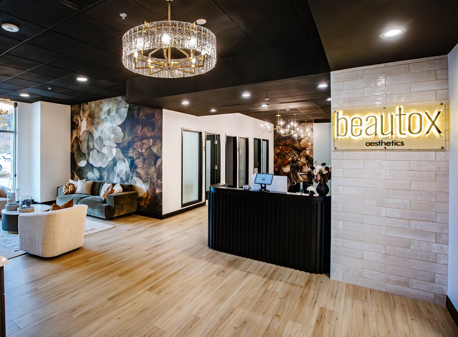 Salon lobby with chandelier, black reception desk, wood floors, and Beautox sign on the wall