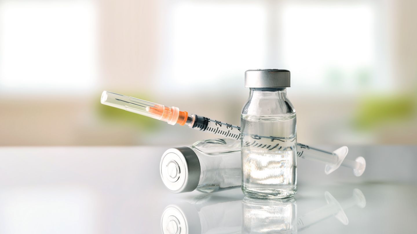 Two bottles of vaccine and a syringe on a table.