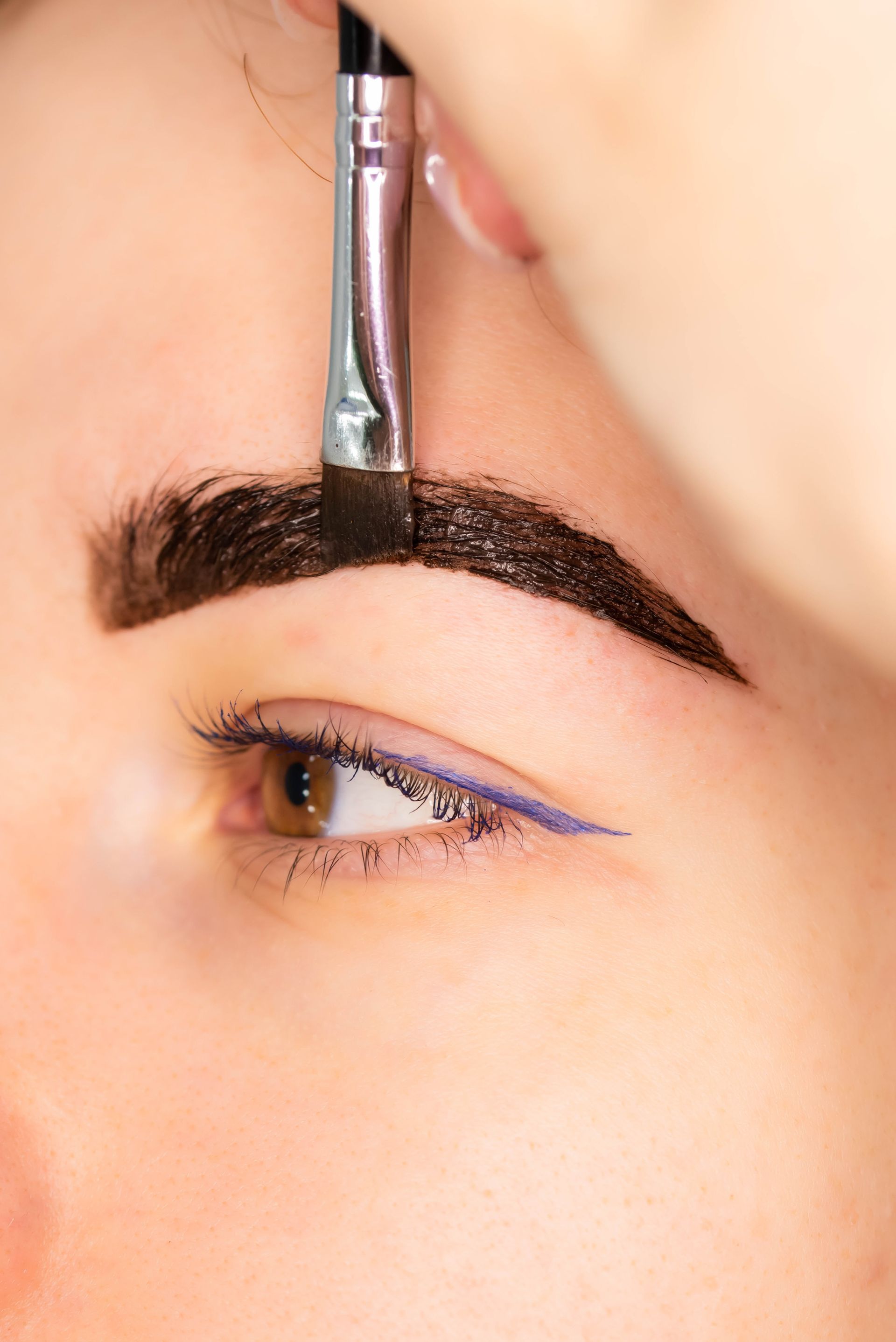 A woman is getting her eyebrows painted with a brush.