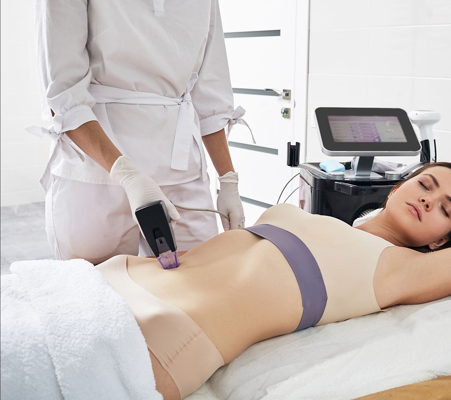 A woman is laying on a bed getting a laser treatment on her stomach.