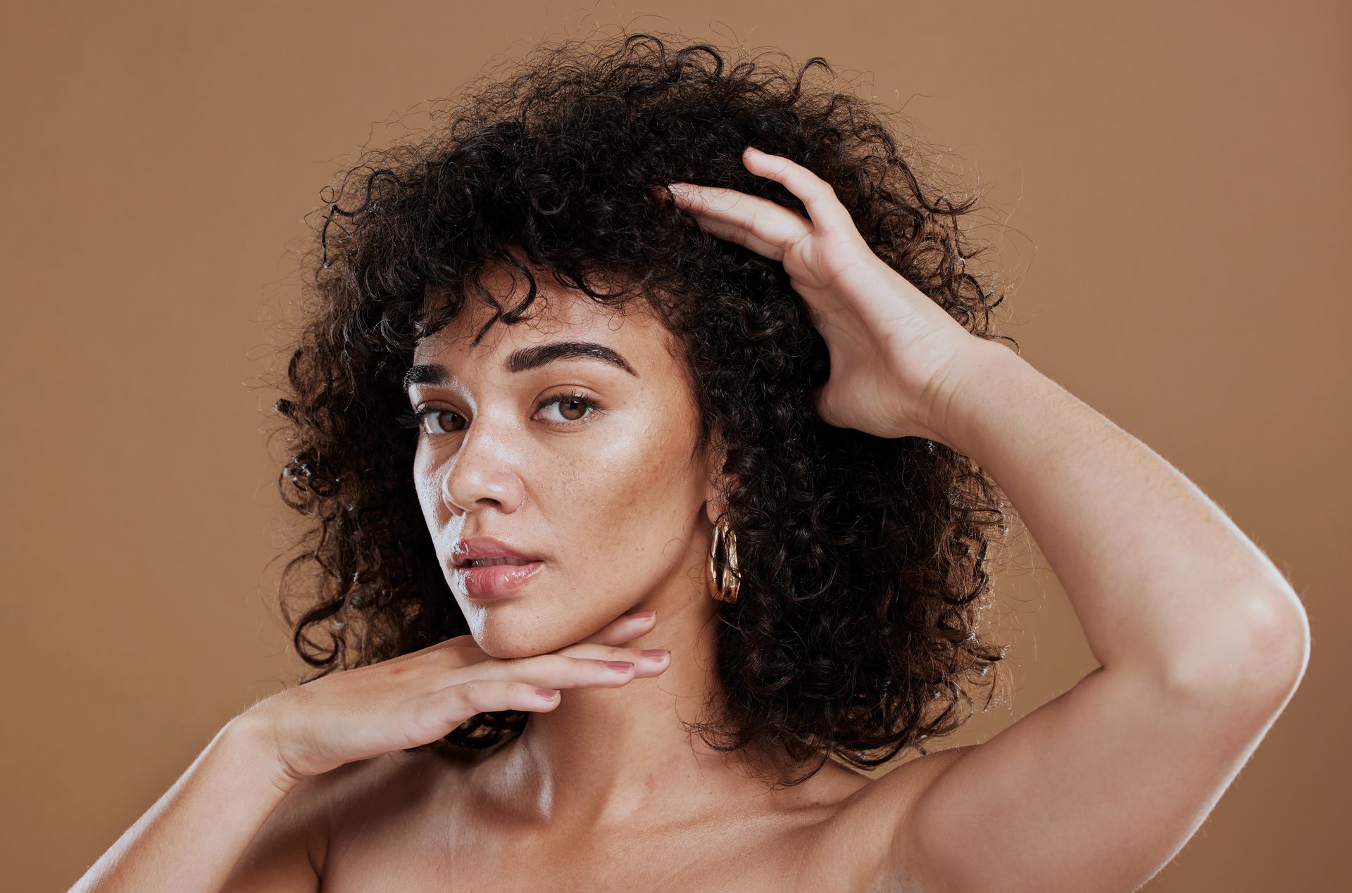 A woman with curly hair is touching her head with her hands.