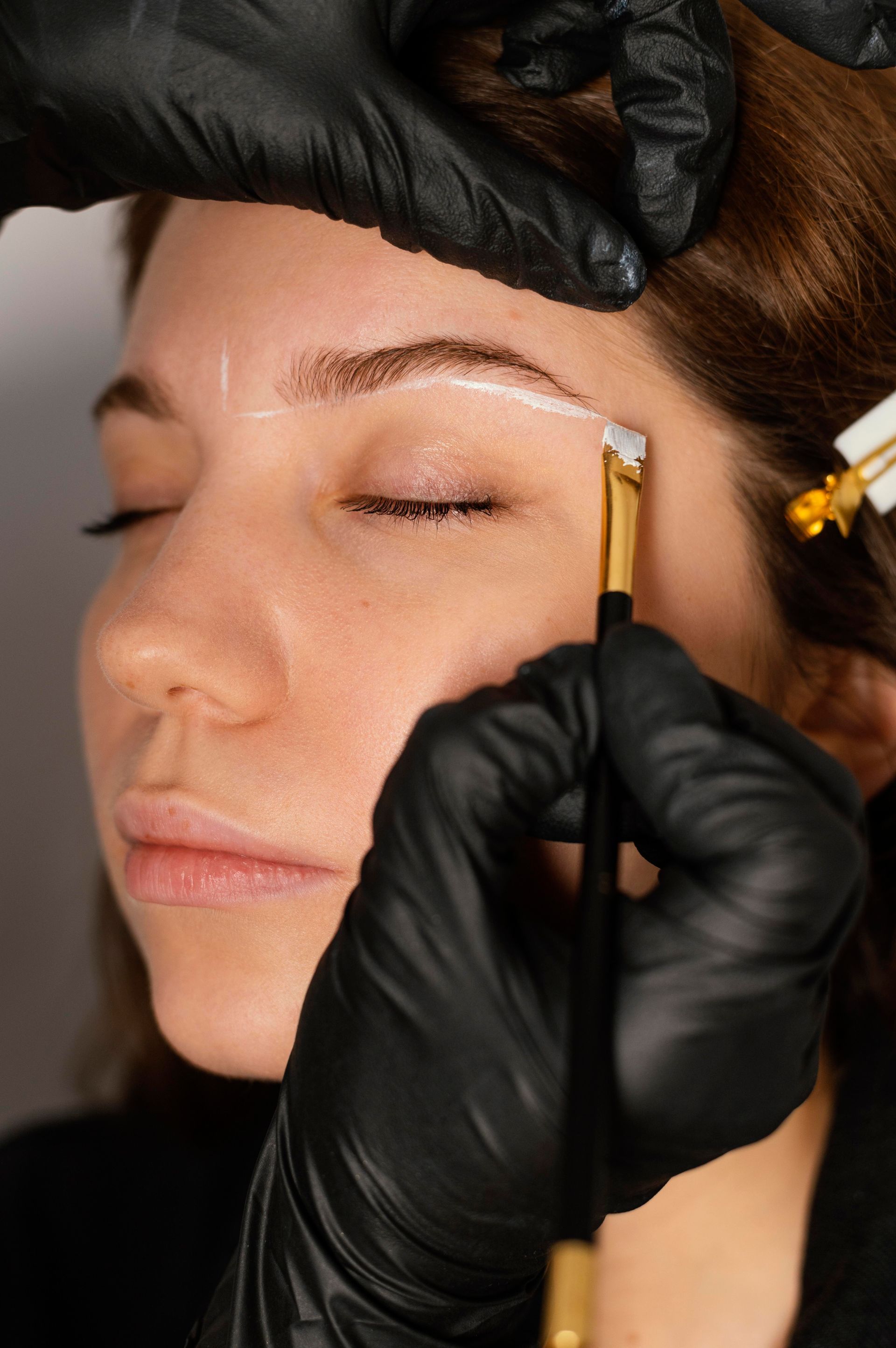 A woman is getting her eyebrows done by a person wearing black gloves.