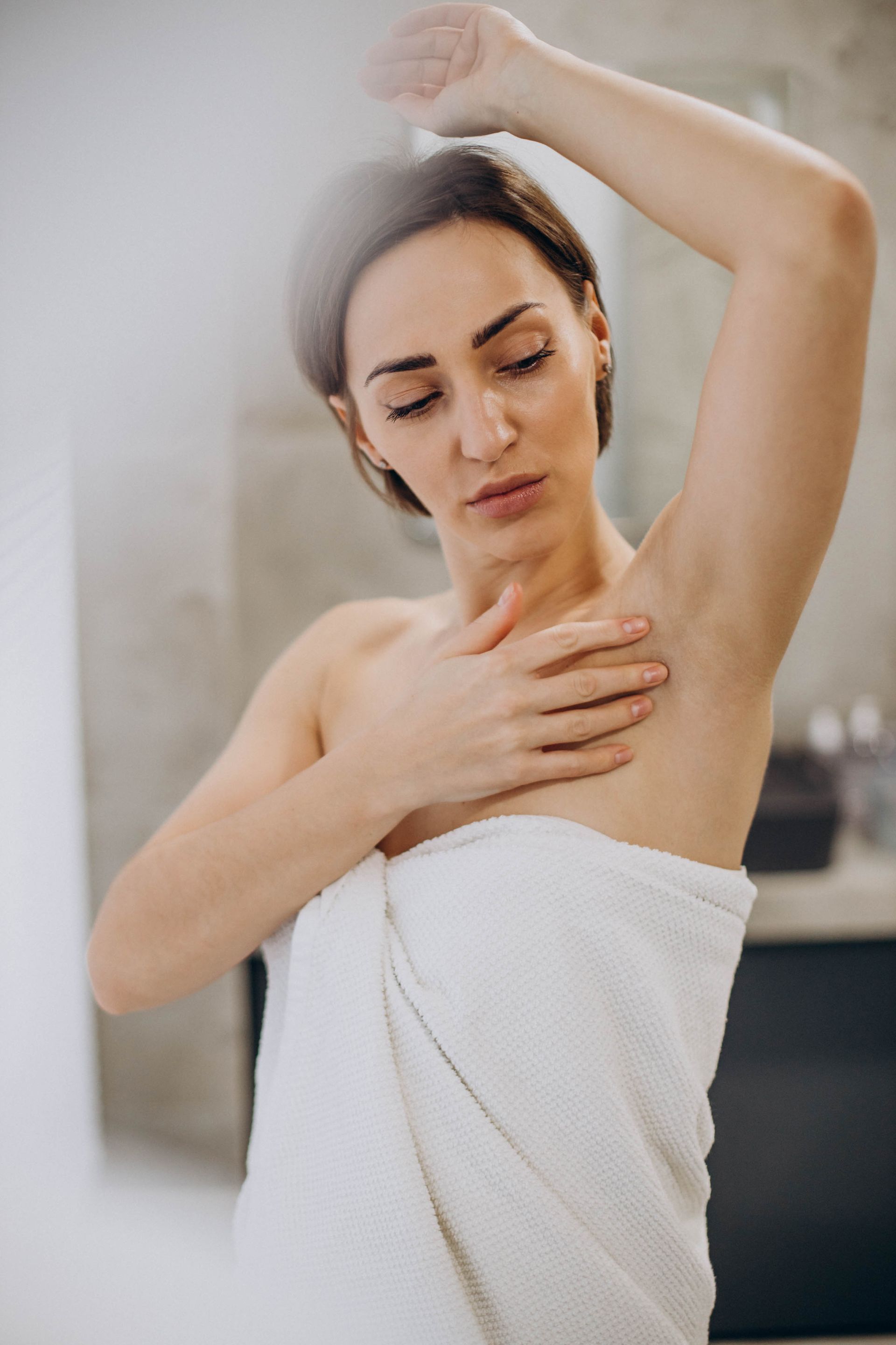 A woman wrapped in a towel is looking at her armpit.