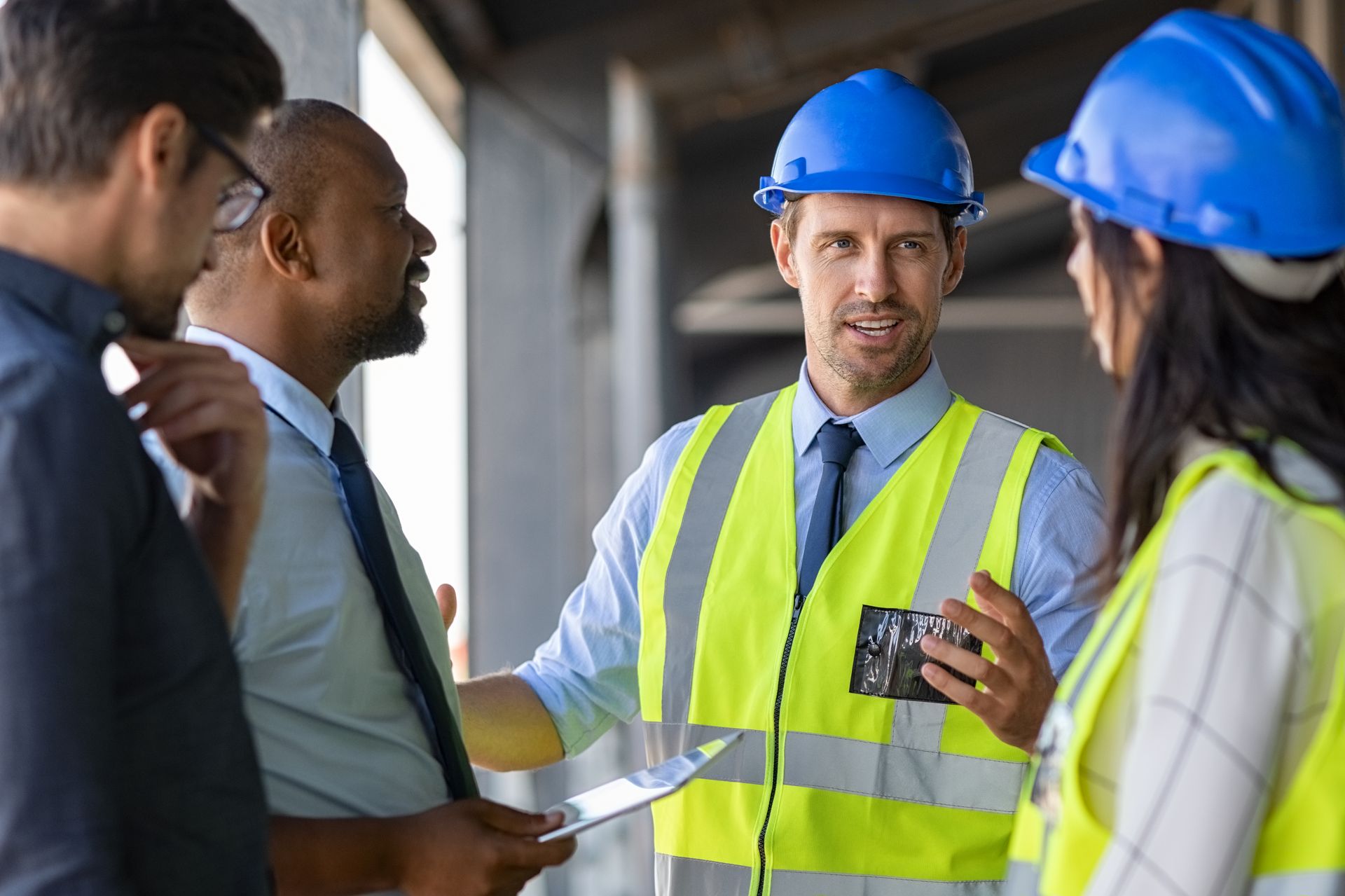Construction workers in hard hats and safety vests discussing a project at a construction site.