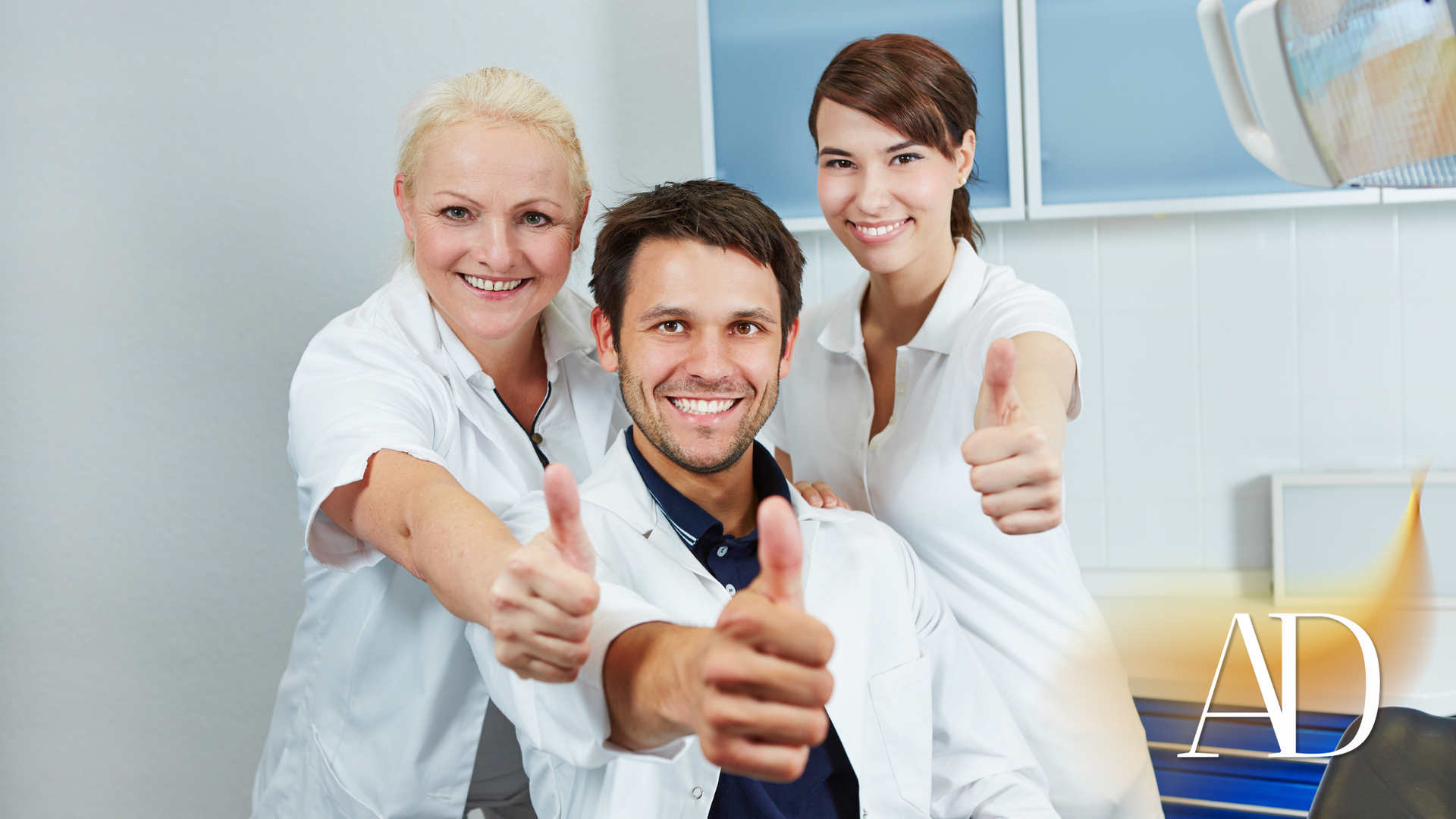 Three smiling medical staff in white coats giving thumbs-up in a bright clinic