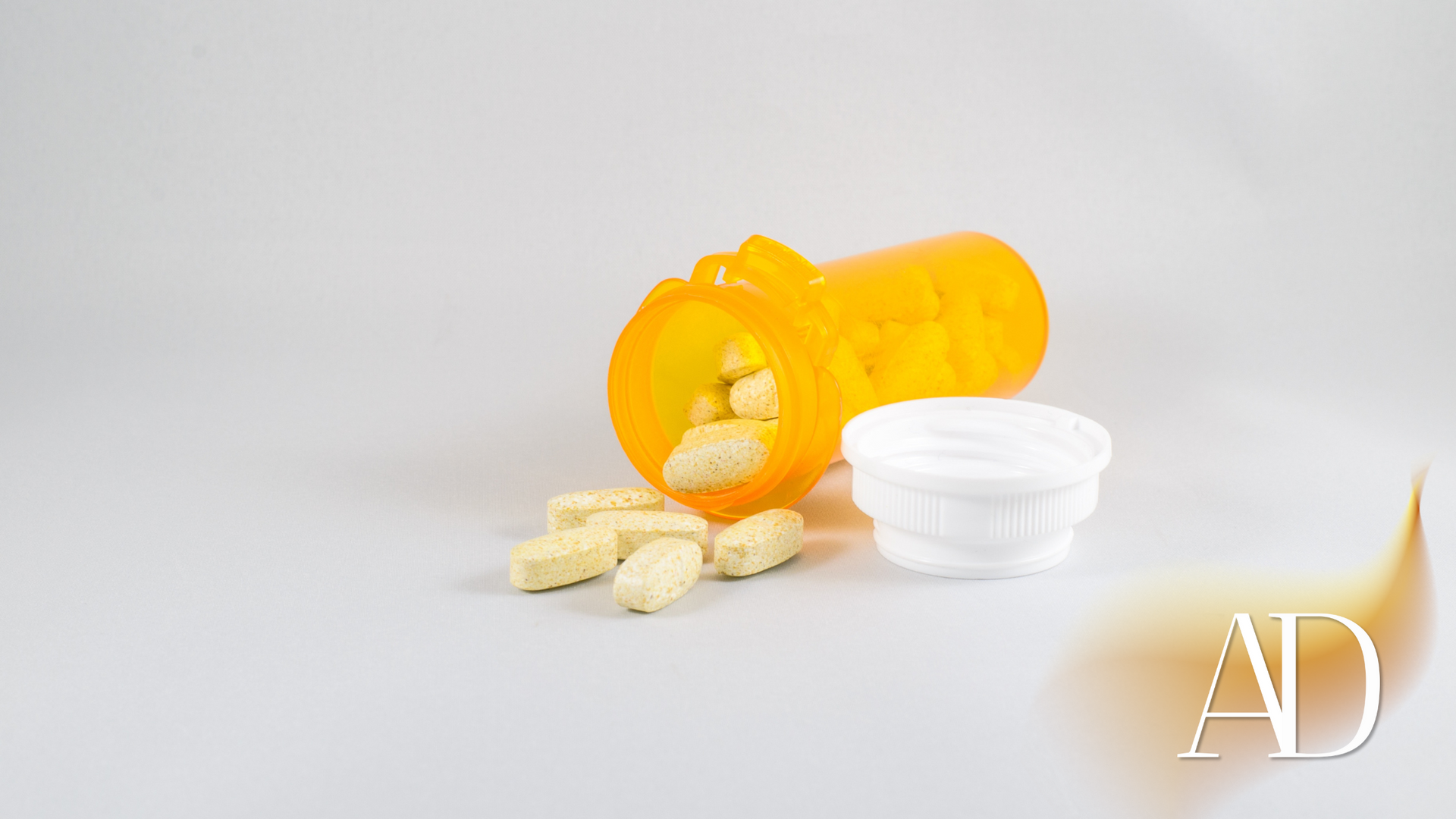 Yellow pill bottle with spilled white tablets and a white cap on a light background