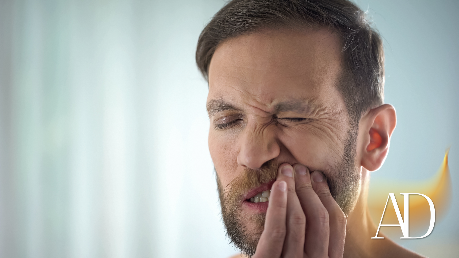 Man holding his cheek in pain, eyes closed, with a toothache
