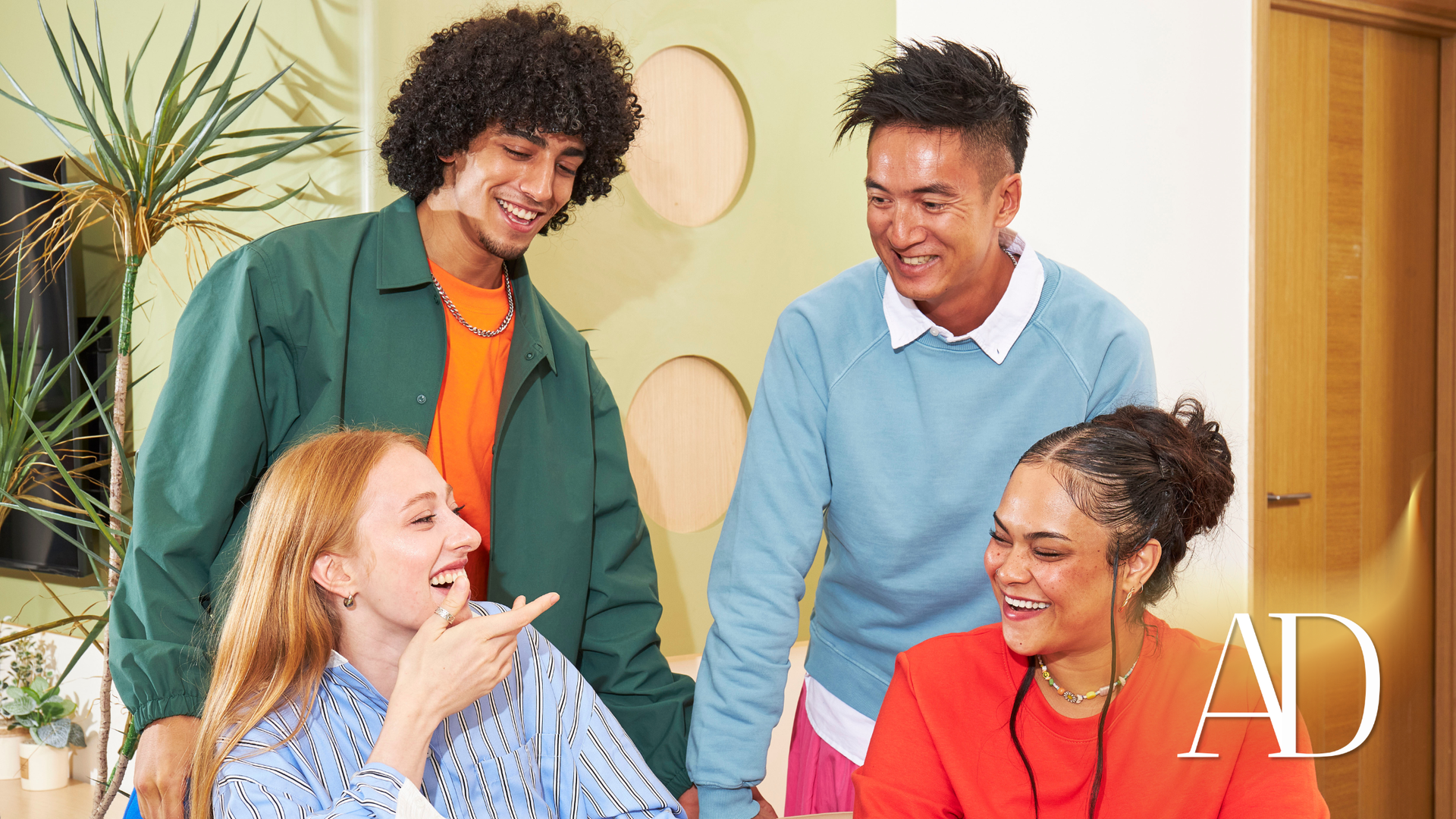 Four coworkers smiling and chatting in a bright office lounge area