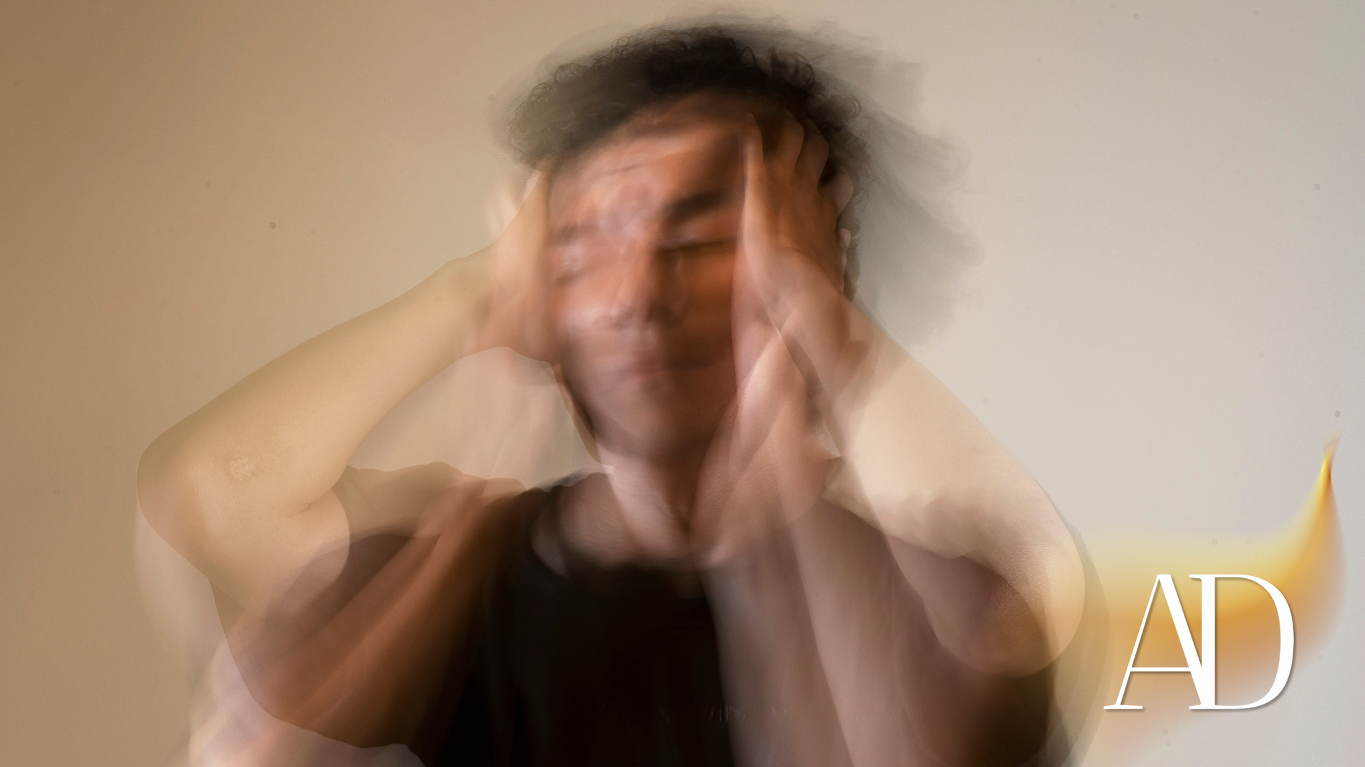 Blurred person holding their head in distress against a plain beige background.