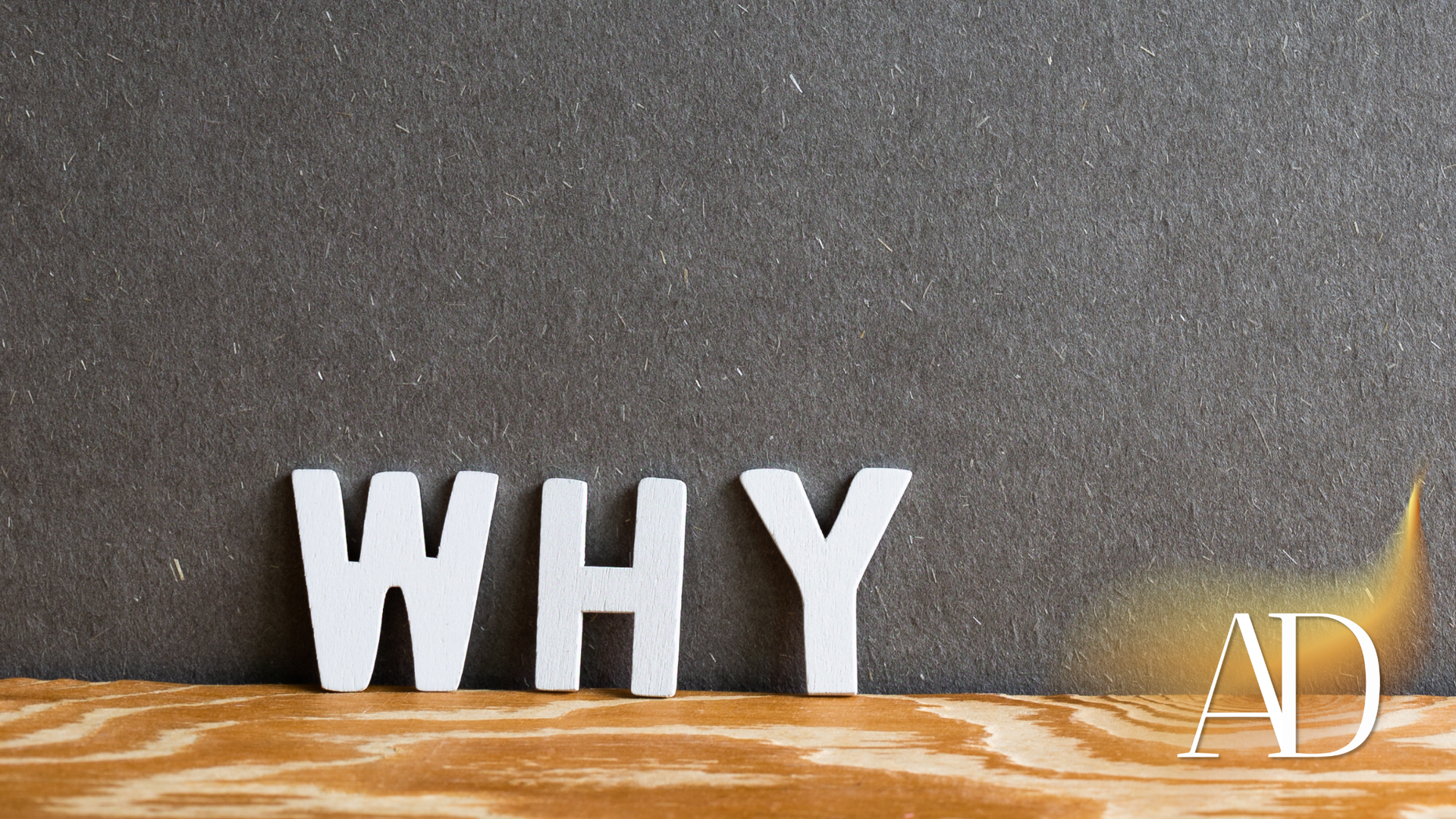 White letters spelling “WHY” on a wooden surface against a dark textured background.
