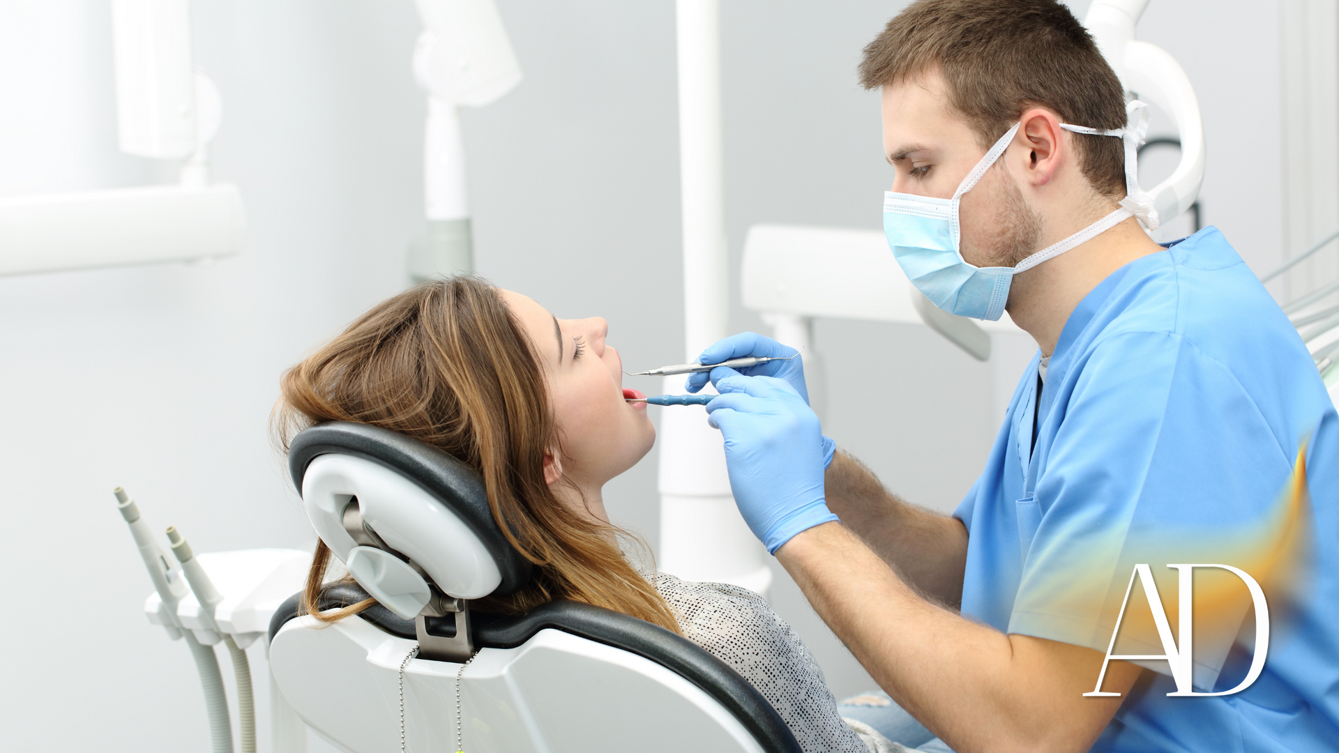 Dentist in blue scrubs examining a patient in a dental chair with tools in hand