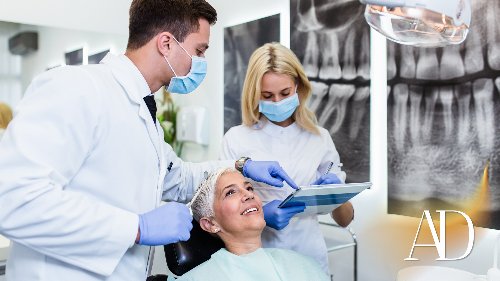 Dentist and assistant treating a patient in a dental clinic, with X-rays visible in the background