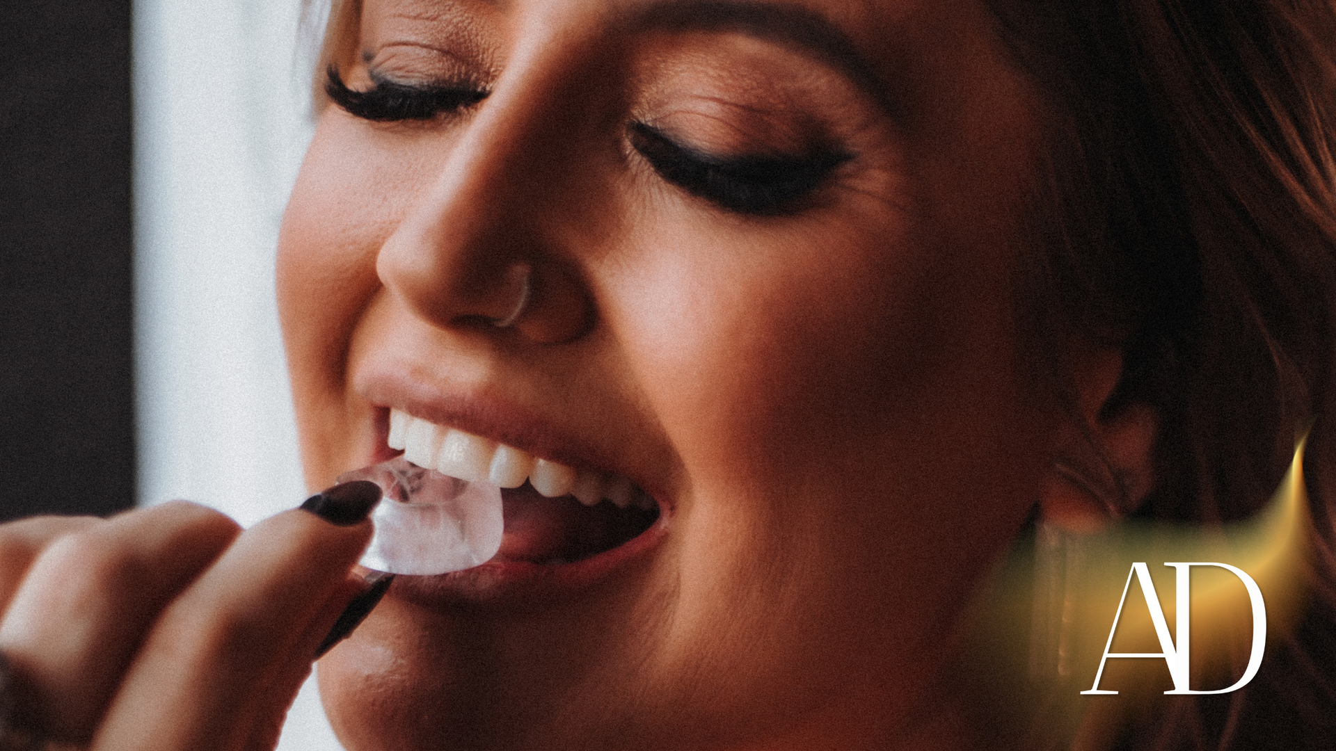 Close-up of a person applying white lipstick with a brush, eyes closed, with AD watermark