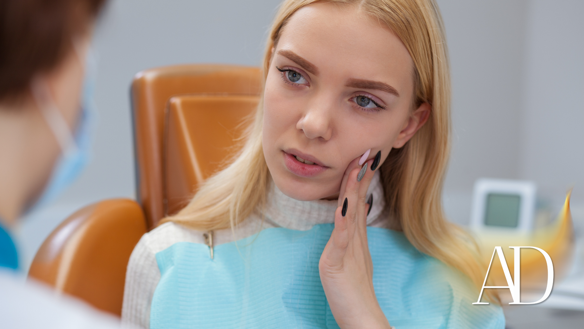 Woman in a blue top touching her cheek during a dental consultation