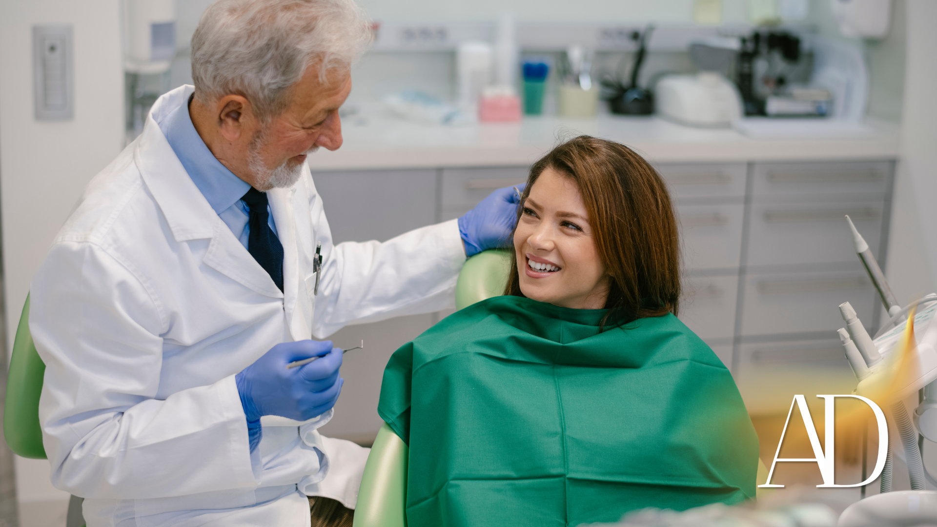 Dentist in white coat talks with smiling patient in green bib in a bright exam room