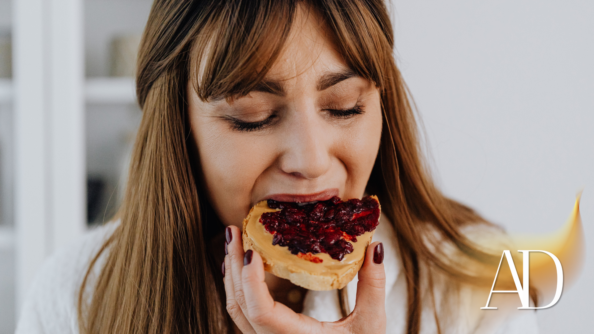 Woman biting into a slice of toast topped with dark red jam