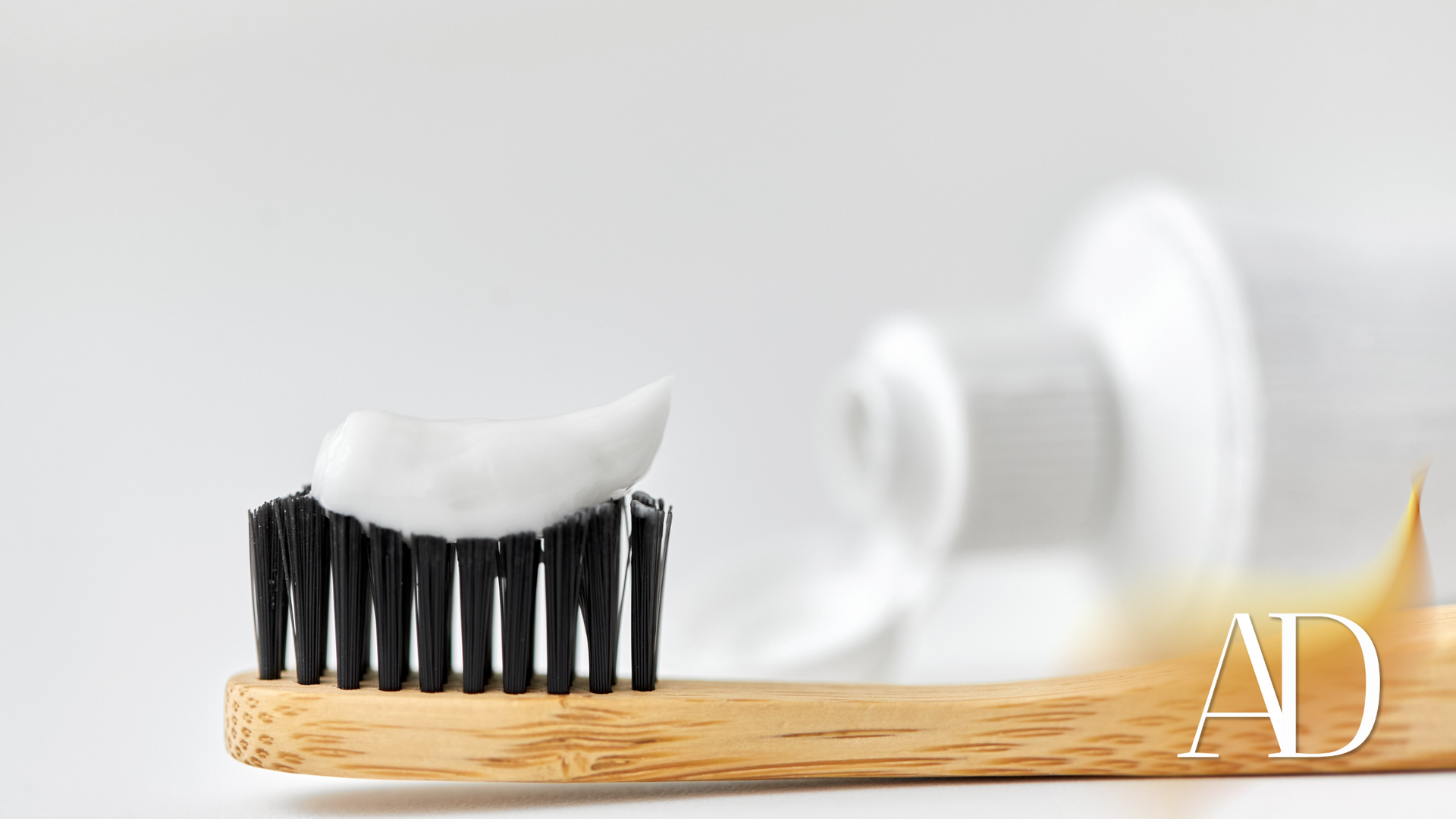 White toothpaste on a black-bristled toothbrush beside a white tube on a light background