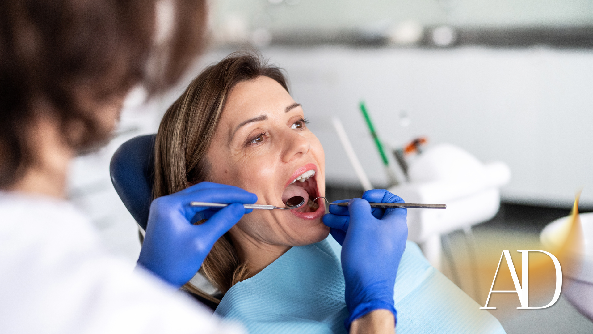 Dentist examining a patient’s open mouth with blue gloves in a dental chair.