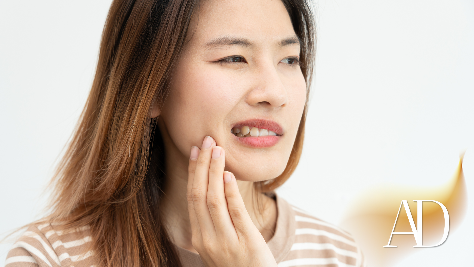 Woman touching her cheek in a bright white setting, with an “AD” watermark in the corner