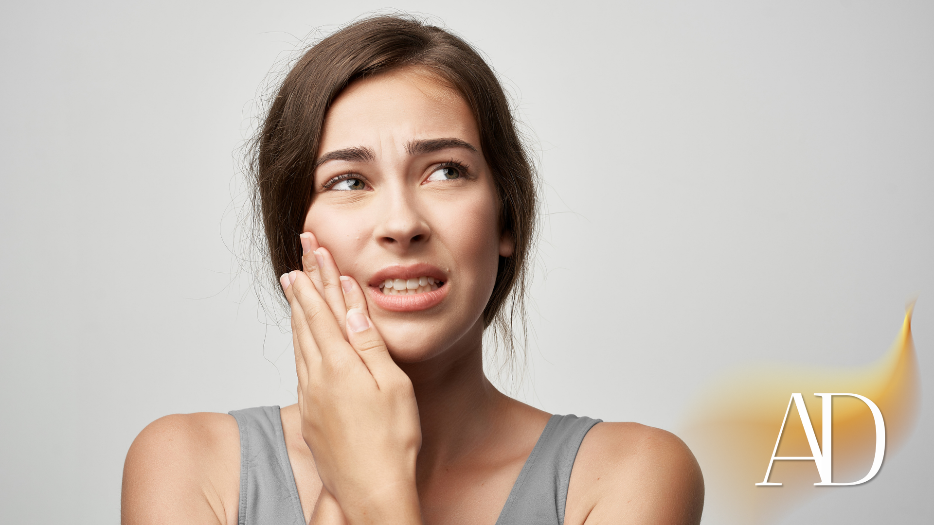 Woman touching her cheek with a worried expression, suggesting tooth or jaw pain, on a light background