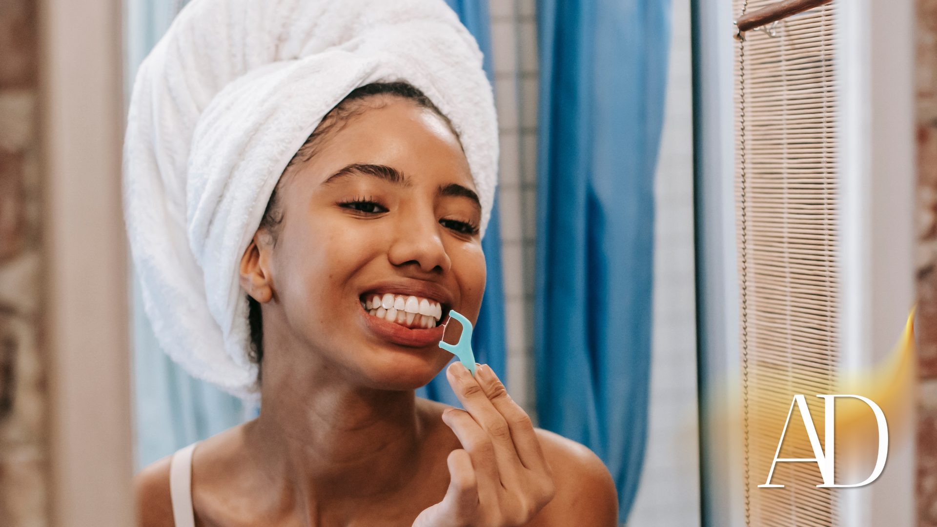 Woman in a towel smiling while applying lip balm in a bathroom mirror.