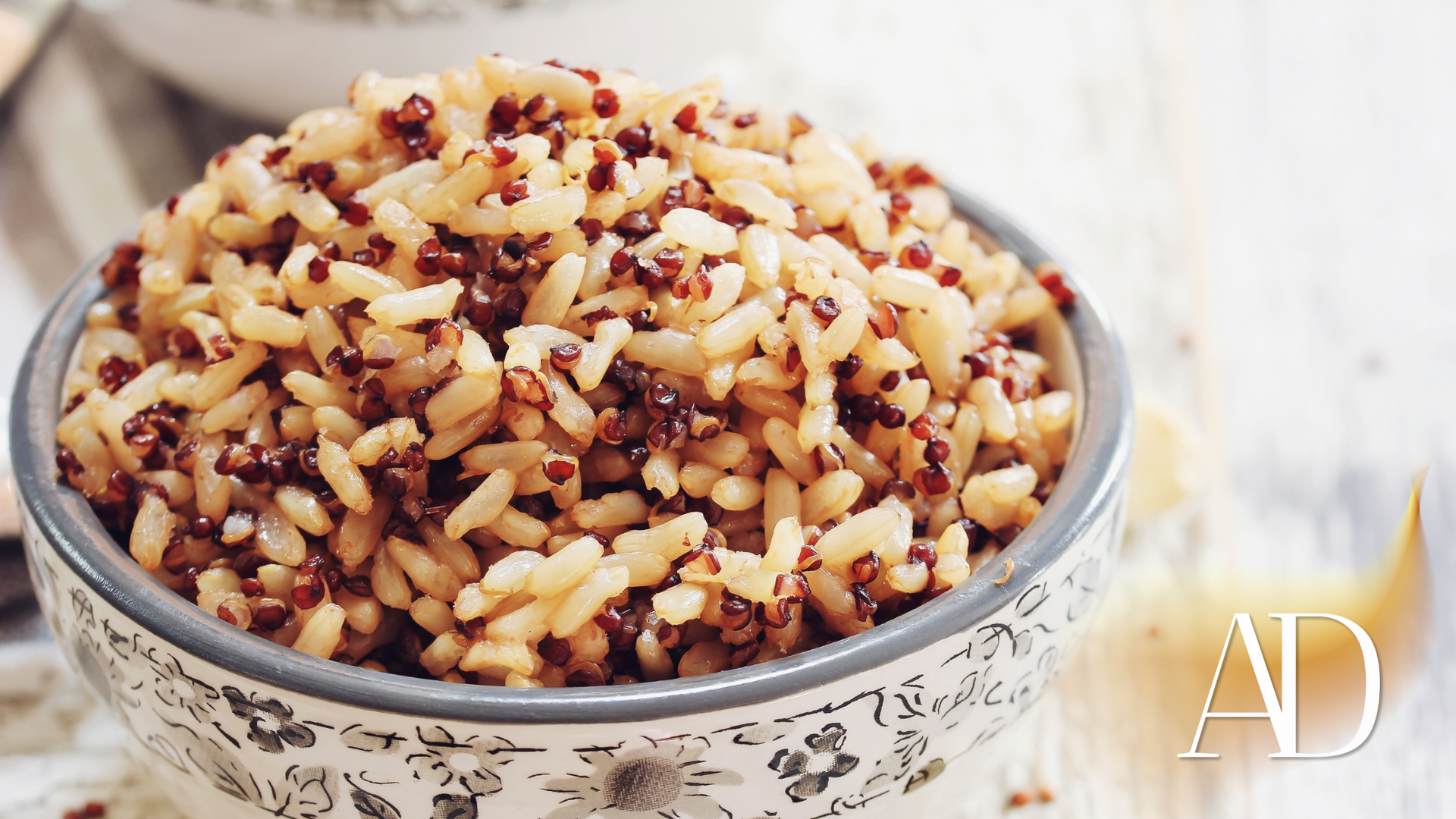 Bowl of rice dish topped with pomegranate seeds and herbs on a light background