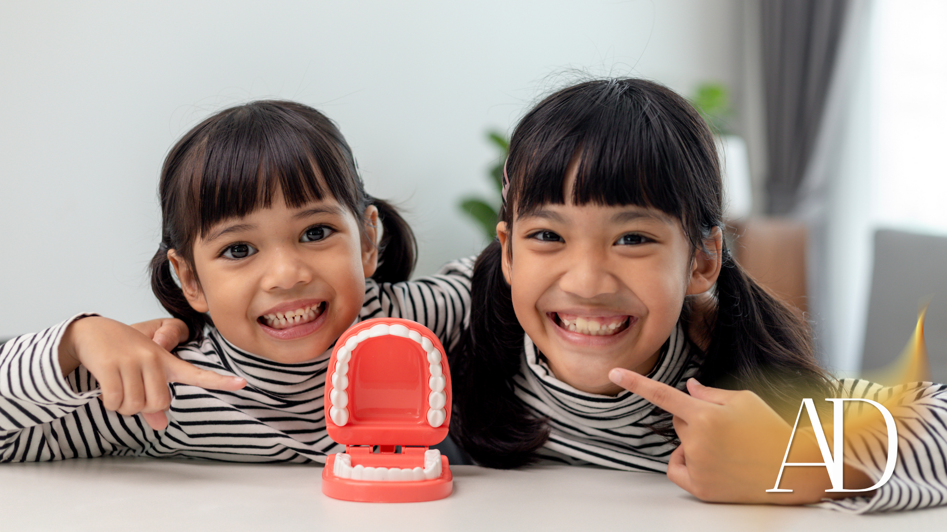 Two smiling children leaning on a table beside a small red toy speaker