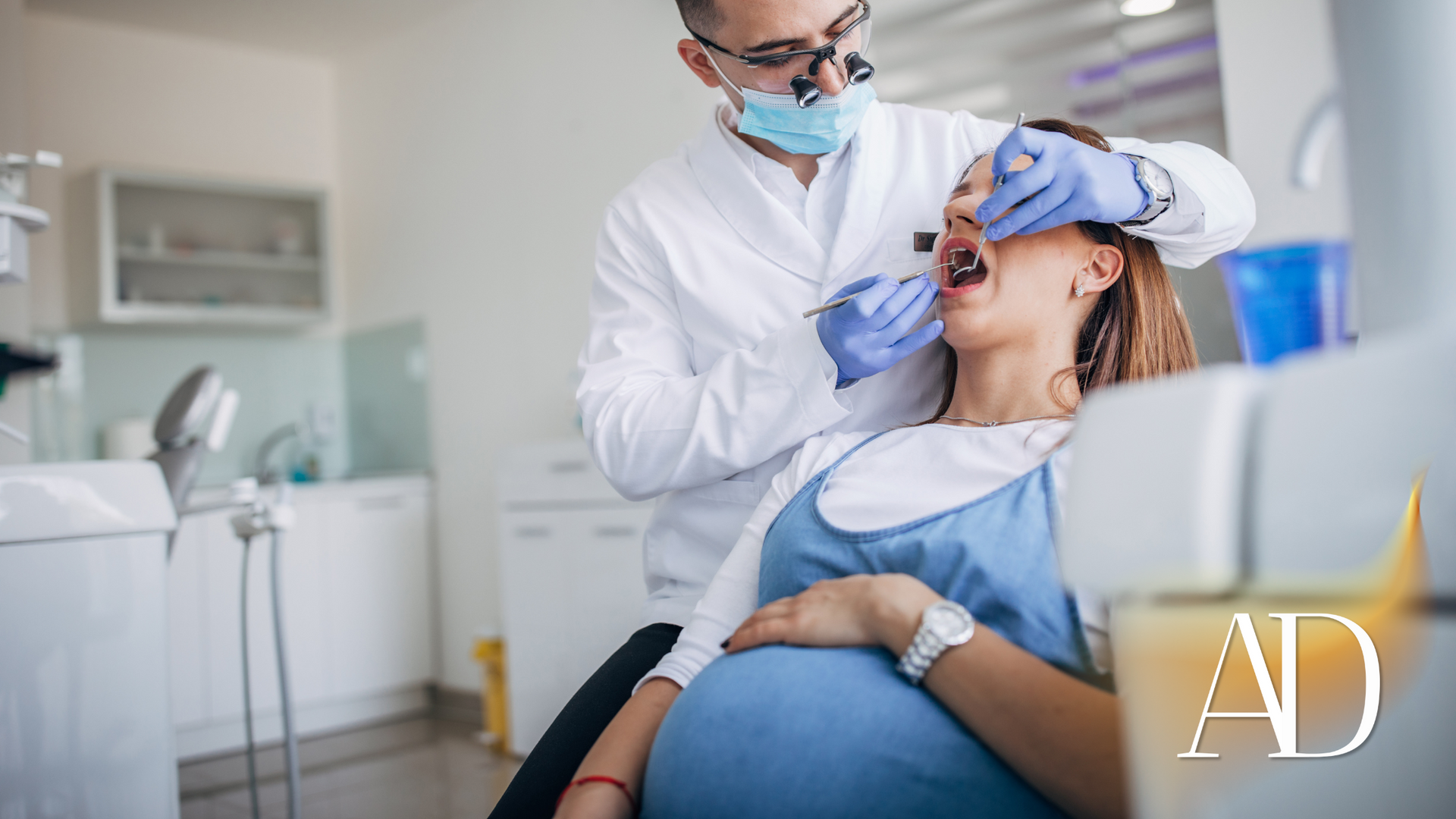 Dentist examining a reclining patient in a bright clinic, using a dental tool and wearing a mask and gloves