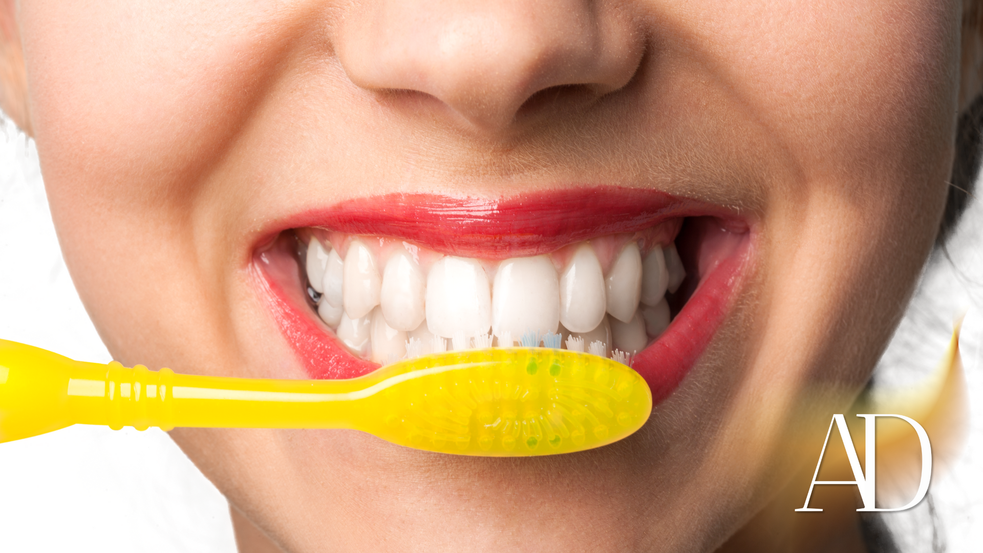 Person brushing white teeth with a yellow toothbrush, smiling close-up