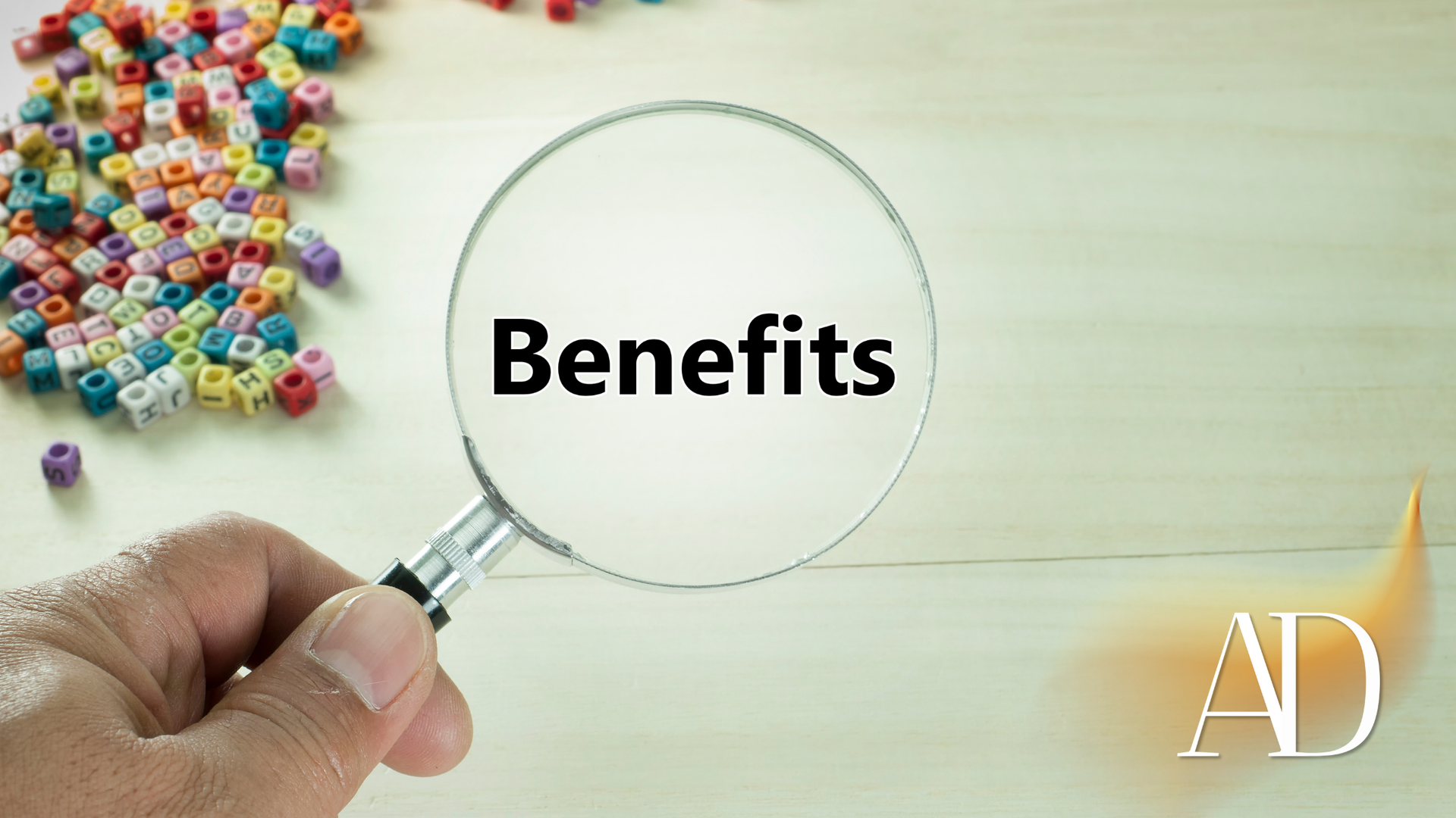 Magnifying glass over the word “Benefits” on a light desk, with colorful beads in the corner