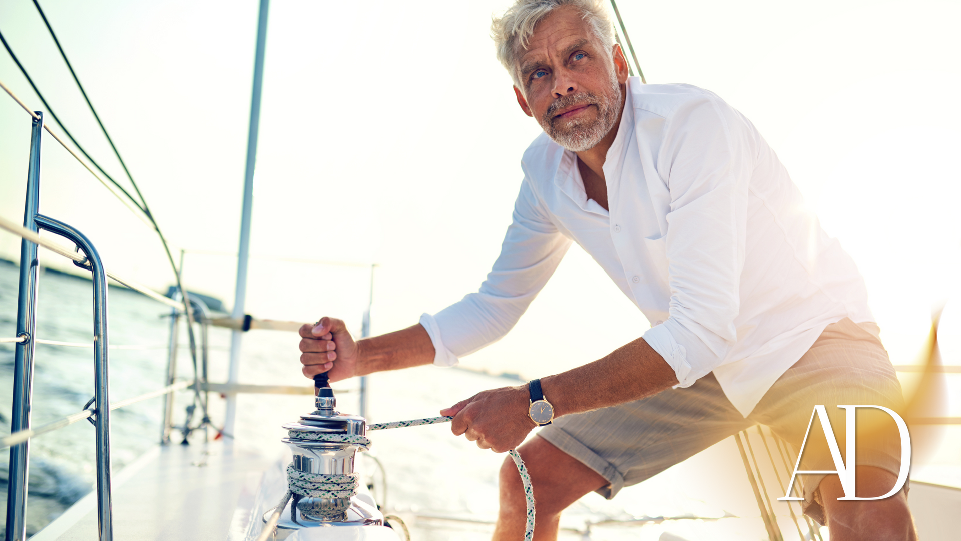 Man in white shirt steering a sailboat on a bright sunny day