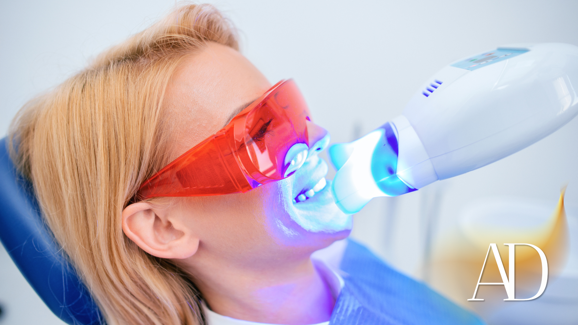 Woman receiving blue-light dental treatment while wearing red protective glasses