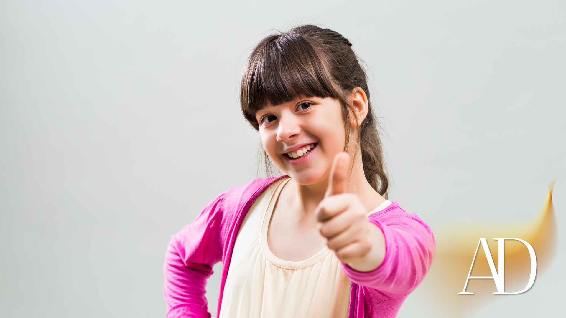 Smiling person in a pink cardigan gives a thumbs-up against a light gray background.