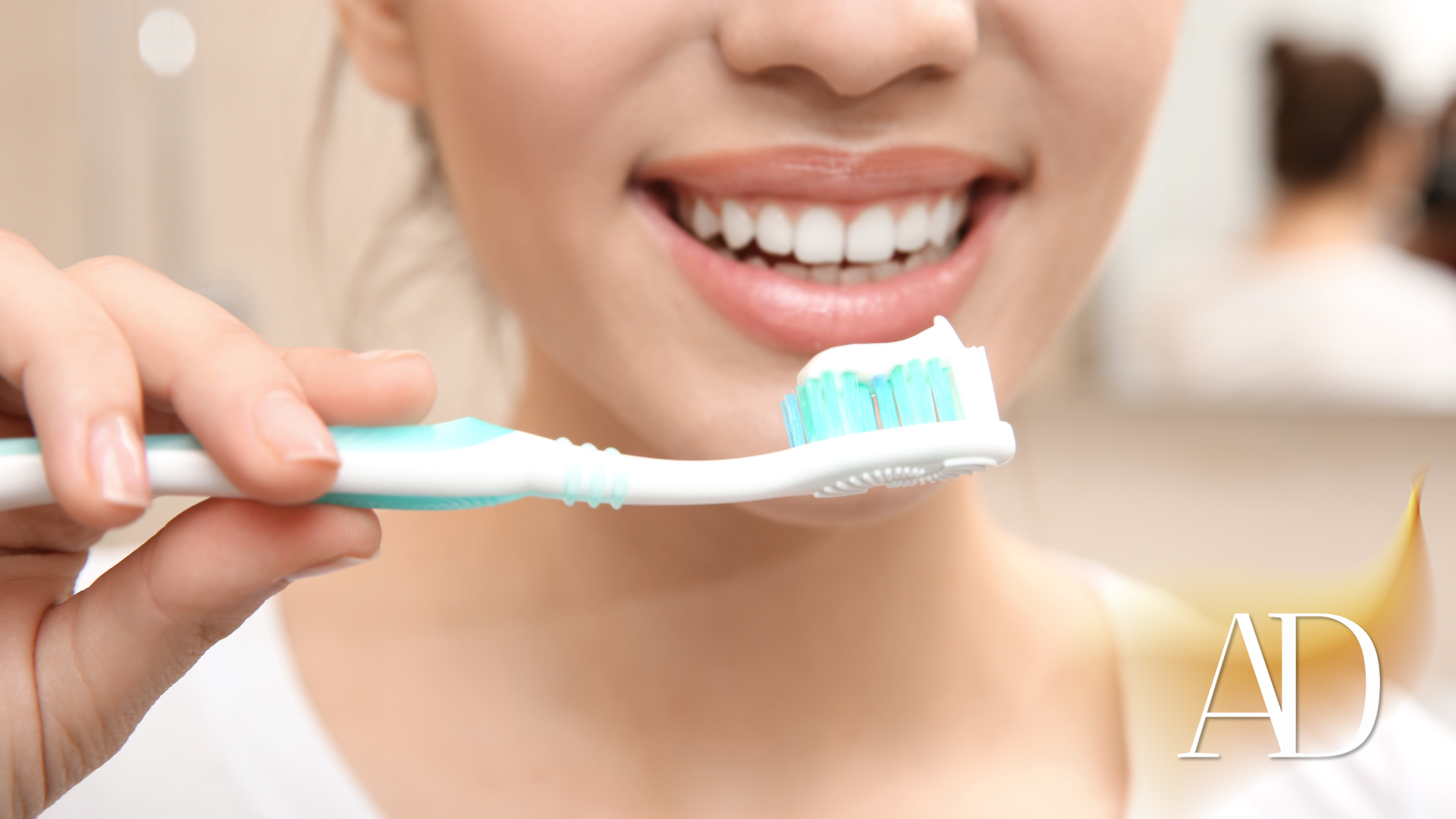 Person brushing teeth with a mint-green toothbrush, smiling in a bathroom mirror.