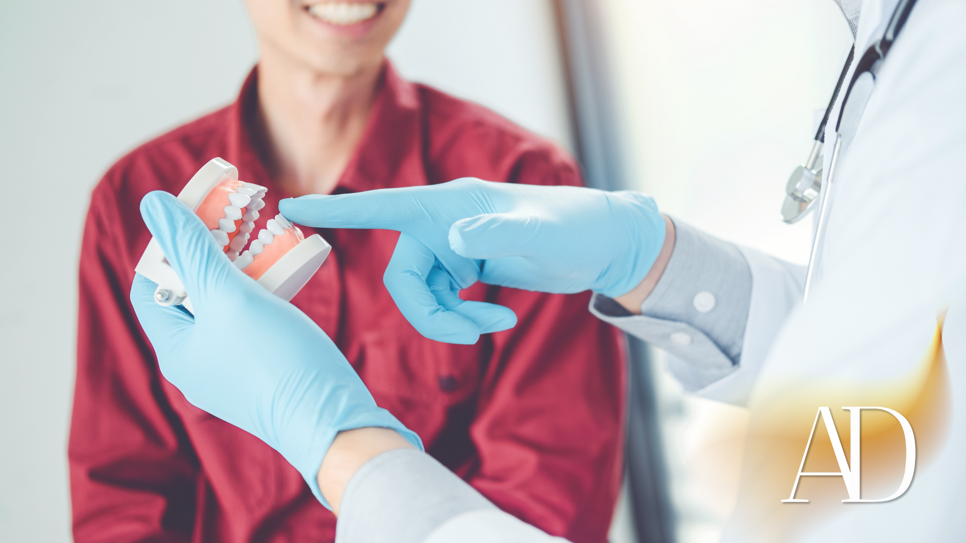Clinician in red scrubs points to a dental model held by blue-gloved hands