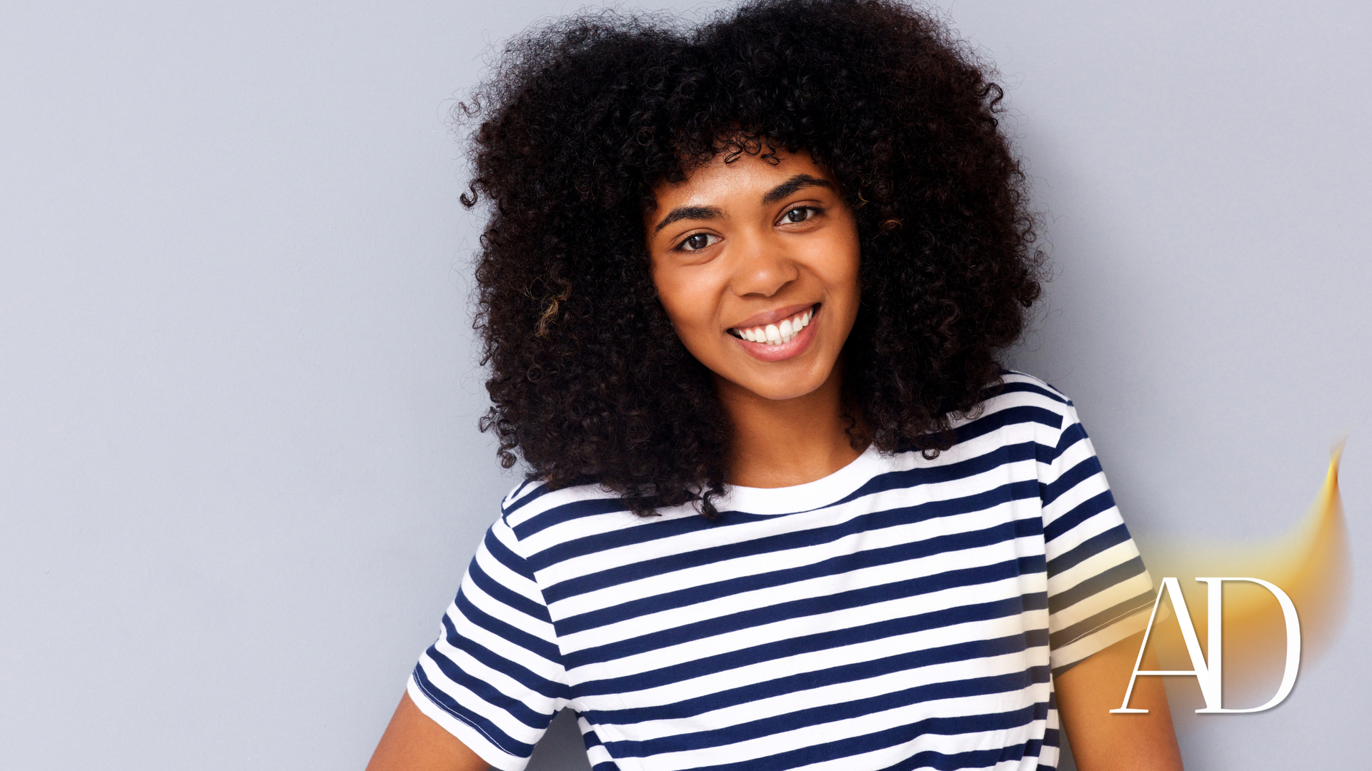 Smiling woman in a navy-and-white striped shirt against a light gray background.
