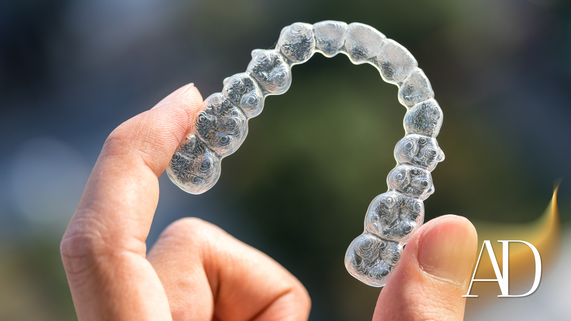 Hand holding a clear dental aligner against a blurred green background