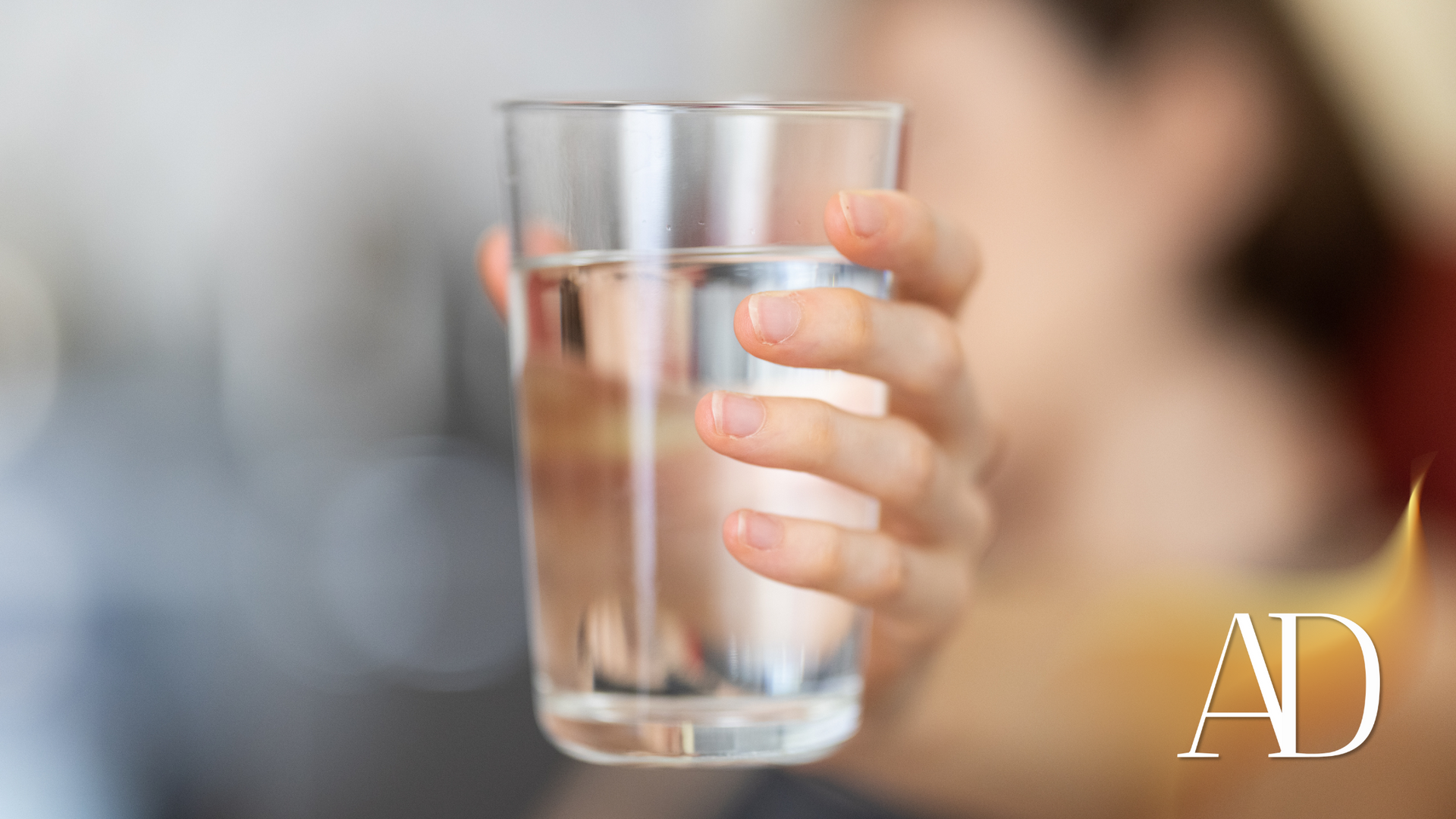 Hand holding a clear glass of water against a blurred background