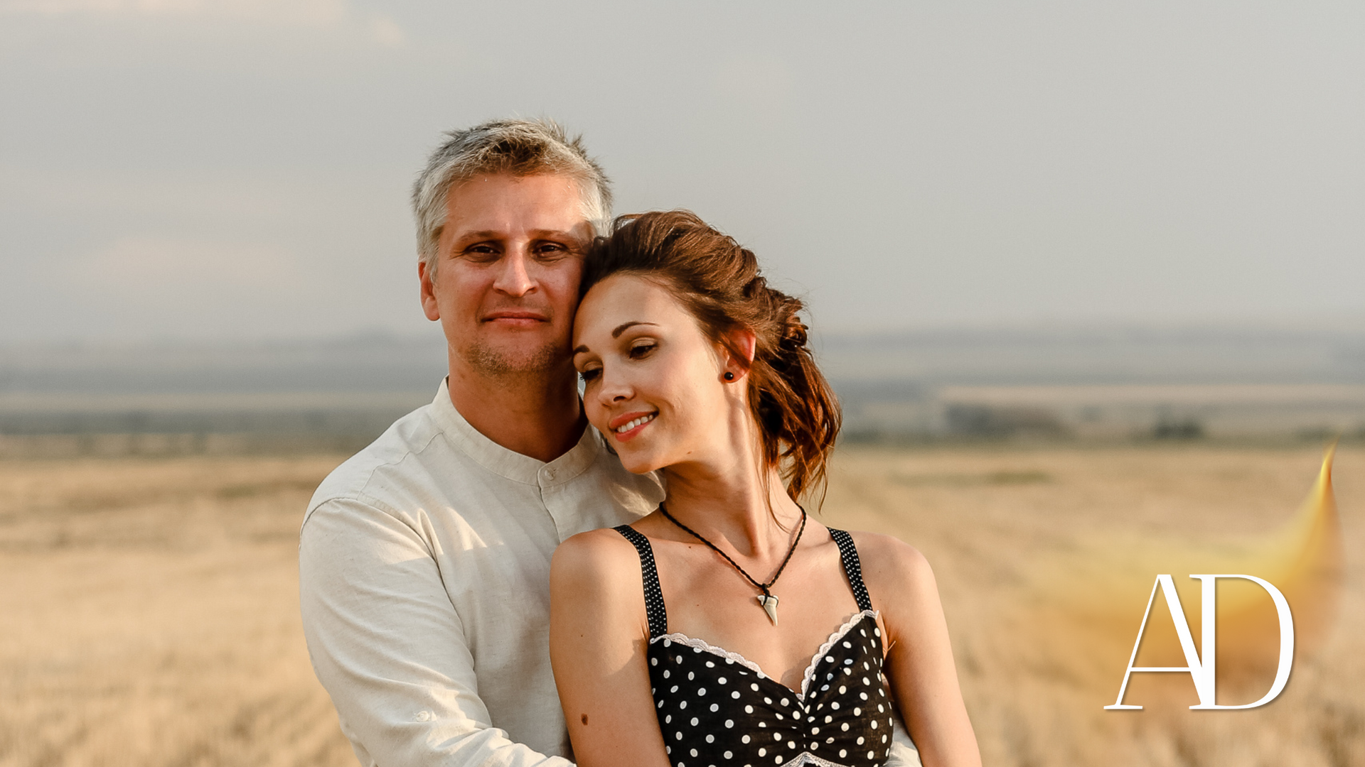 Couple posing together in a sunlit field, with a soft desert landscape in the background.