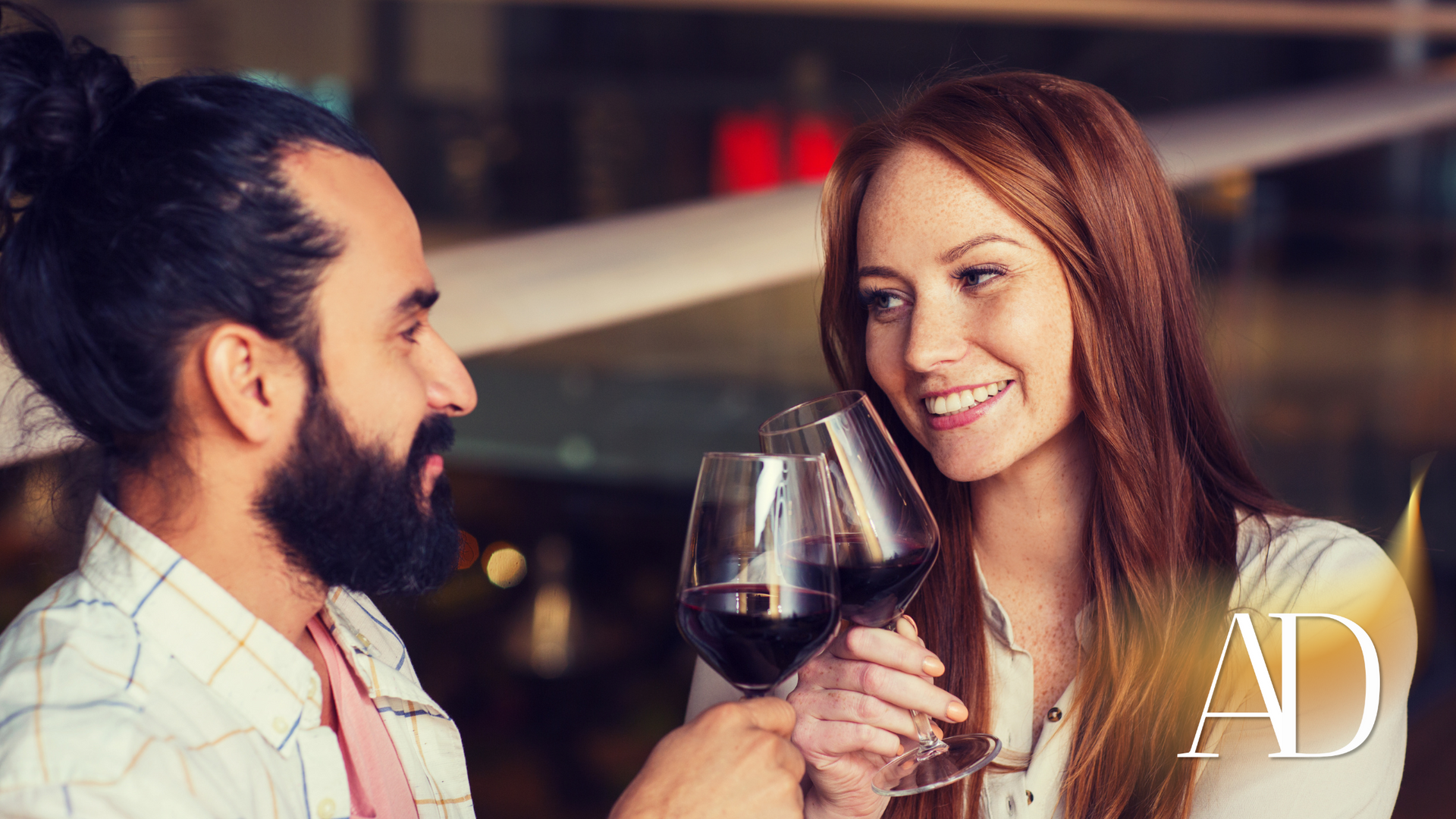 Two people clink glasses of red wine at a softly lit restaurant table
