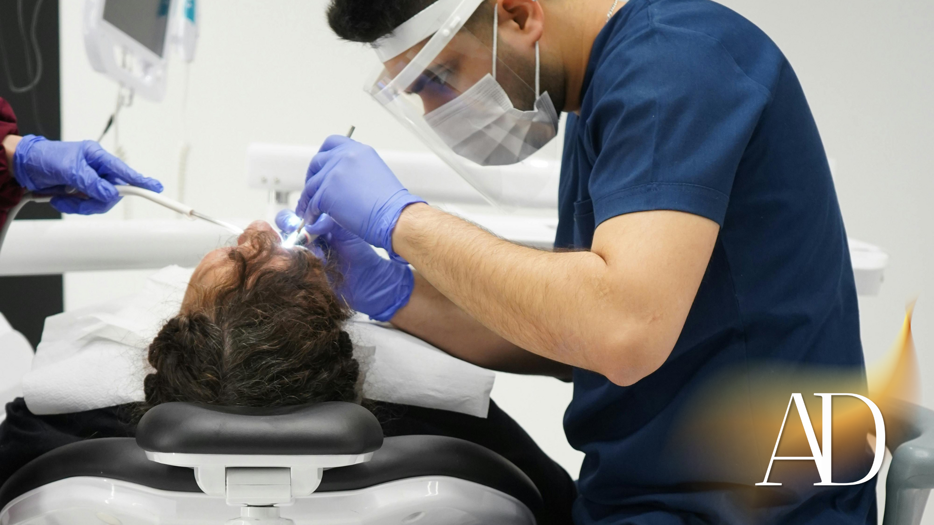 Dentist wearing a face shield and mask treating a patient reclined in a dental chair