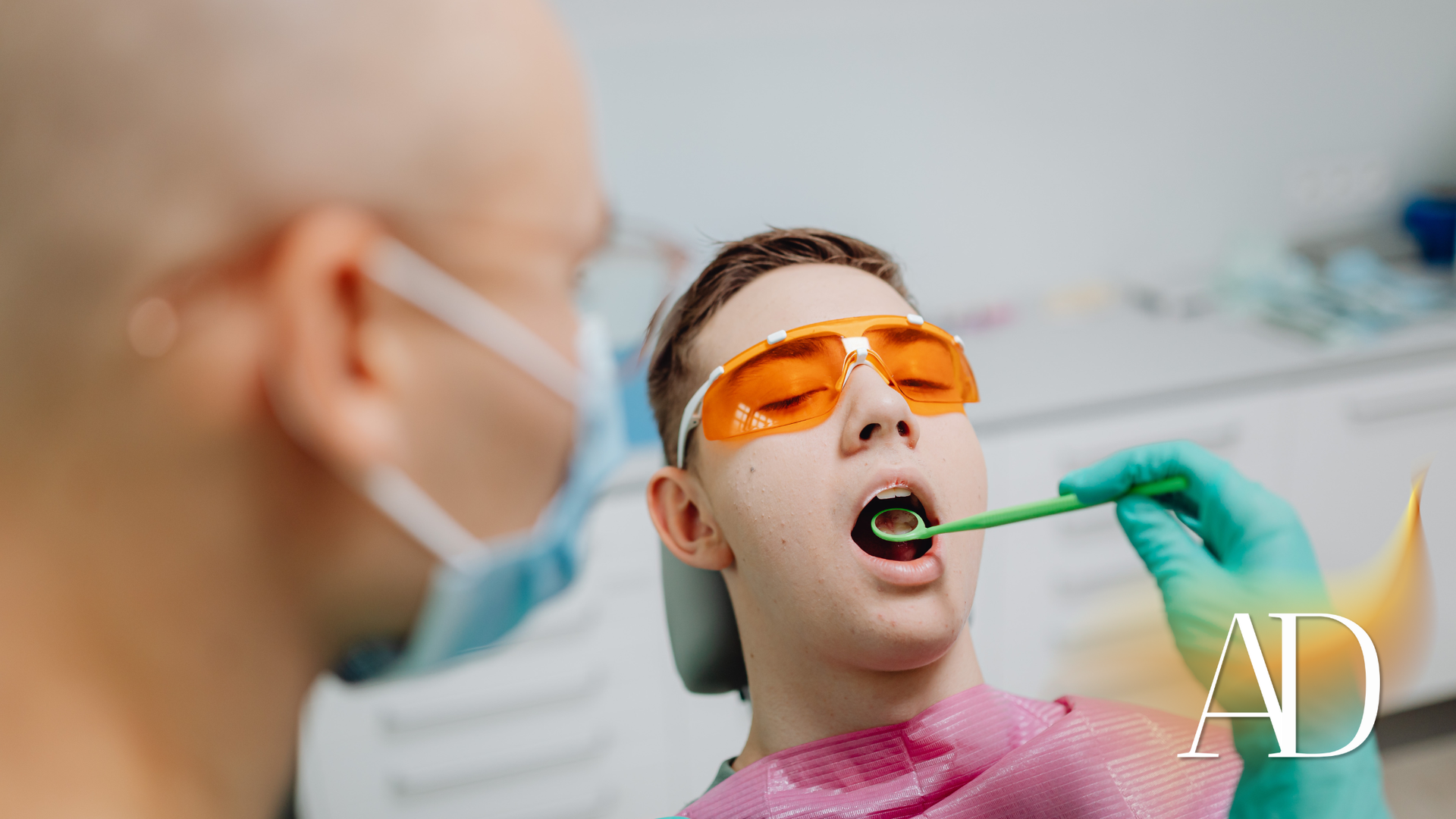 Dentist examining a patient with orange protective glasses as a dental tool reaches into the mouth