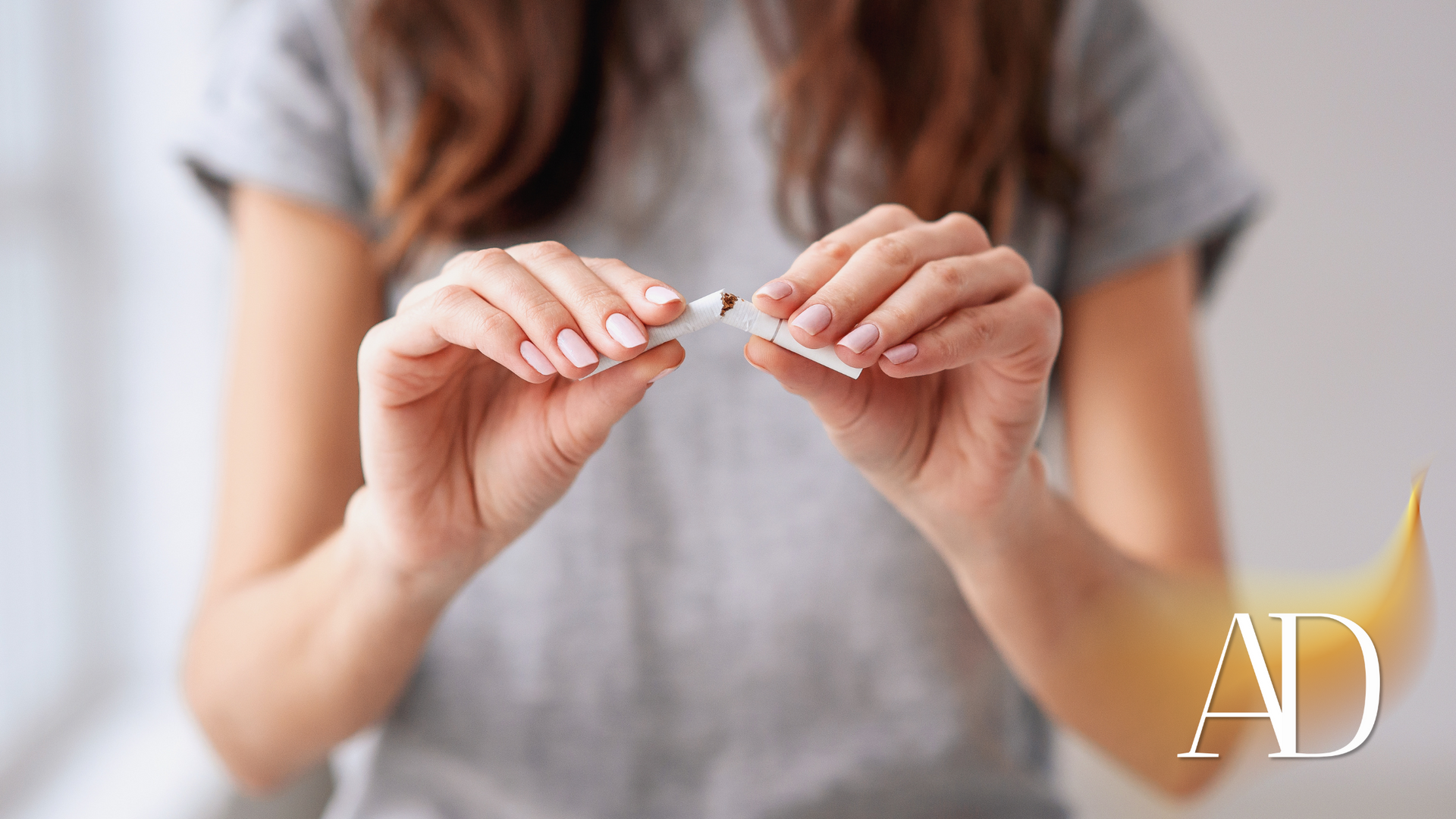 Hands holding a small white item over a gray shirt, with a softly blurred indoor background.