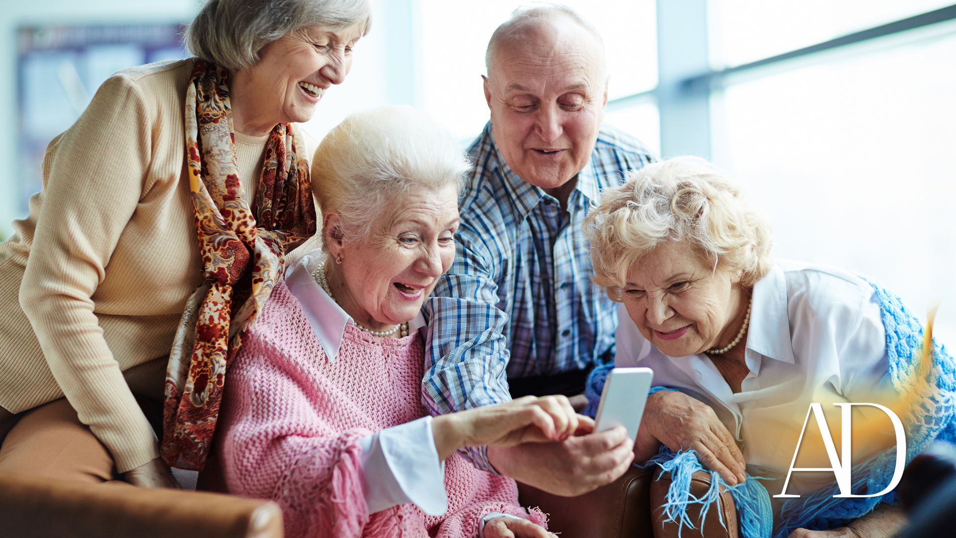 Group of seniors smiling and looking at a smartphone together on a couch